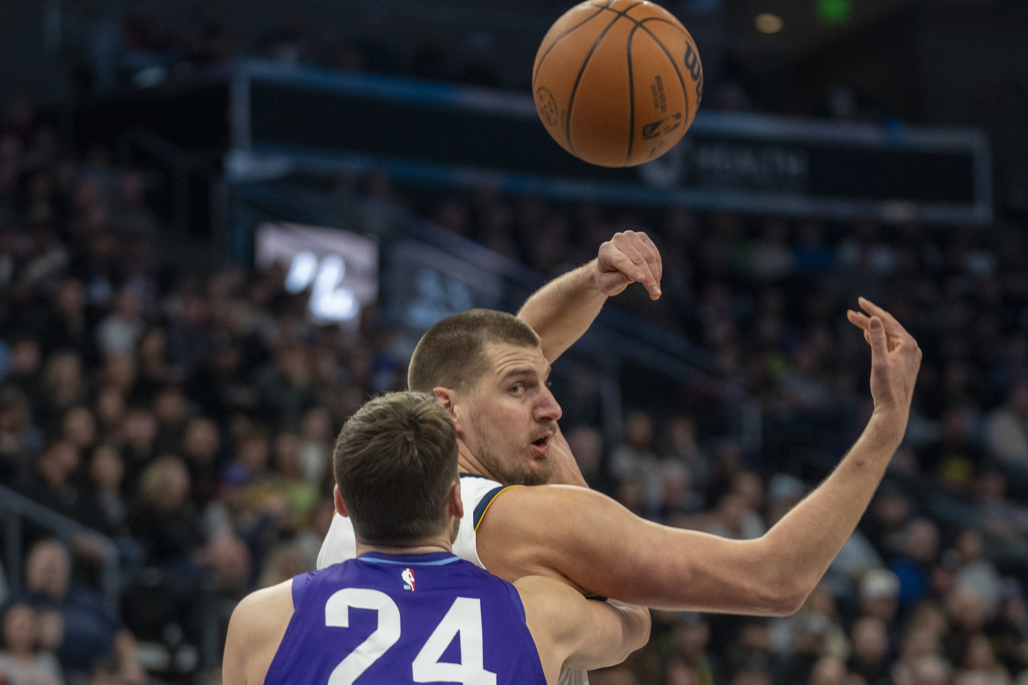 Denver Nuggets center Nikola Jokic, top, tosses a pass over his shoulder as Utah Jazz center Walker Kessler (24) defends during the first half of an NBA basketball game Monday, Dec. 30, 2024, in Salt Lake City.