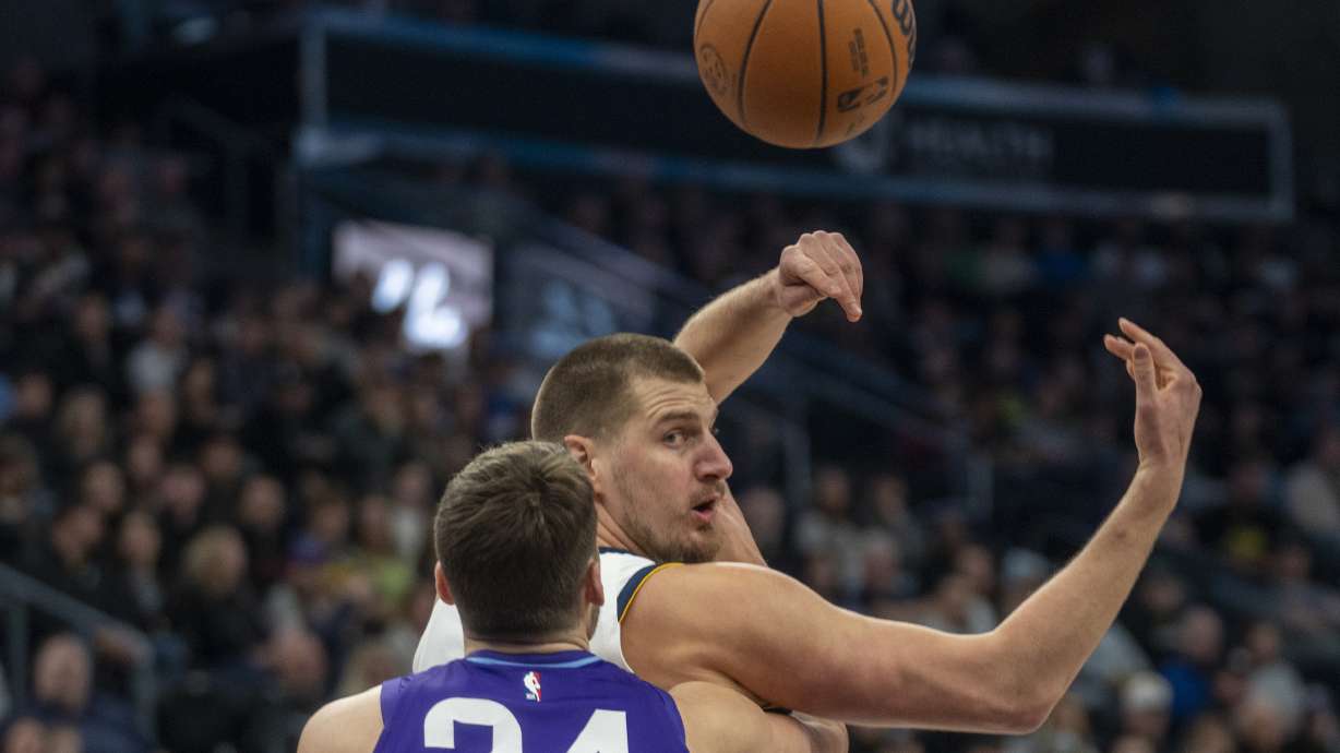 Denver Nuggets center Nikola Jokic, top, tosses a pass over his shoulder as Utah Jazz center Walker Kessler (24) defends during the first half of an NBA basketball game Monday, Dec. 30, 2024, in Salt Lake City.