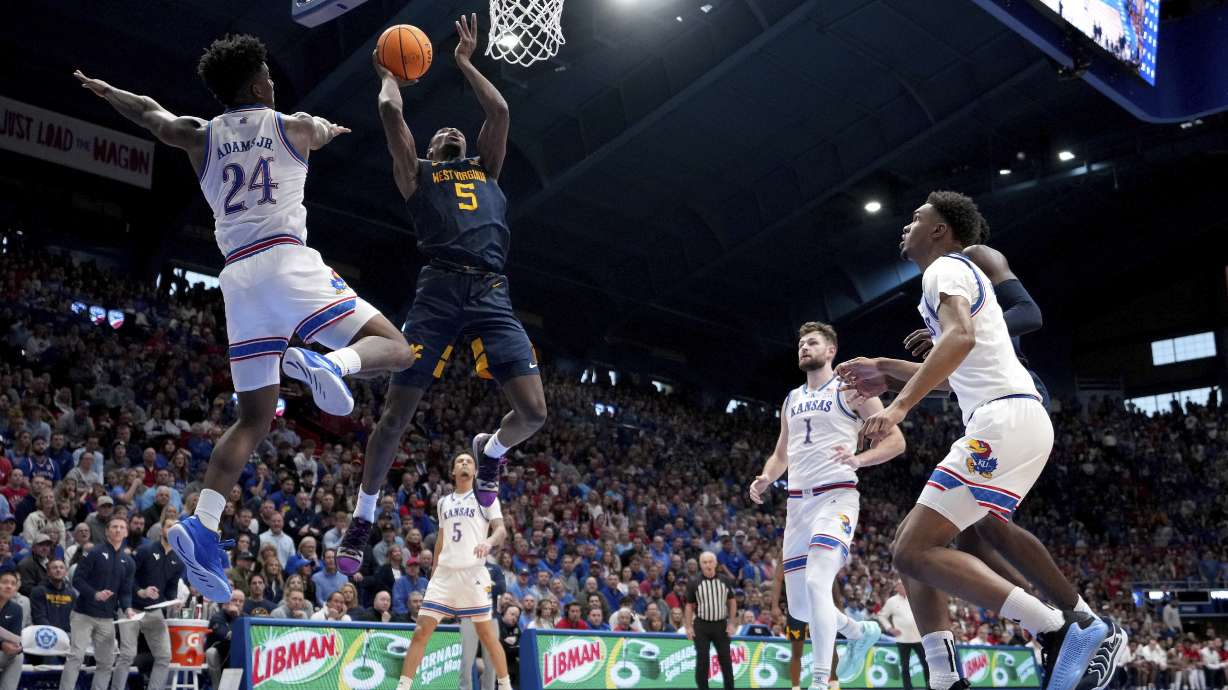 West Virginia guard Toby Okani (5) gets past Kansas forward KJ Adams Jr. (24) to put up a shot during the second half of an NCAA college basketball game, Tuesday, Dec. 31, 2024, in Lawrence, Kan. West Virginia won 62-61