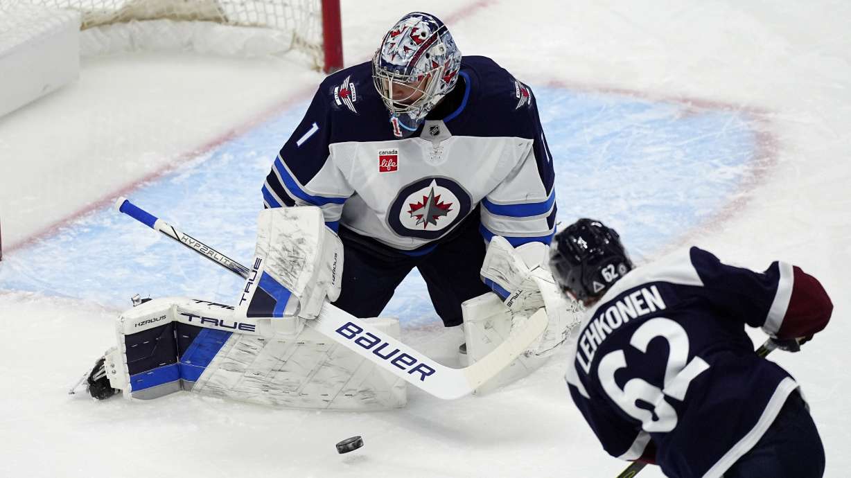 Winnipeg Jets goaltender Eric Comrie, back, makes a pad save of a shot from Colorado Avalanche left wing Artturi Lehkonen in the first period of an NHL hockey game Tuesday, Dec. 31, 2024, in Denver.