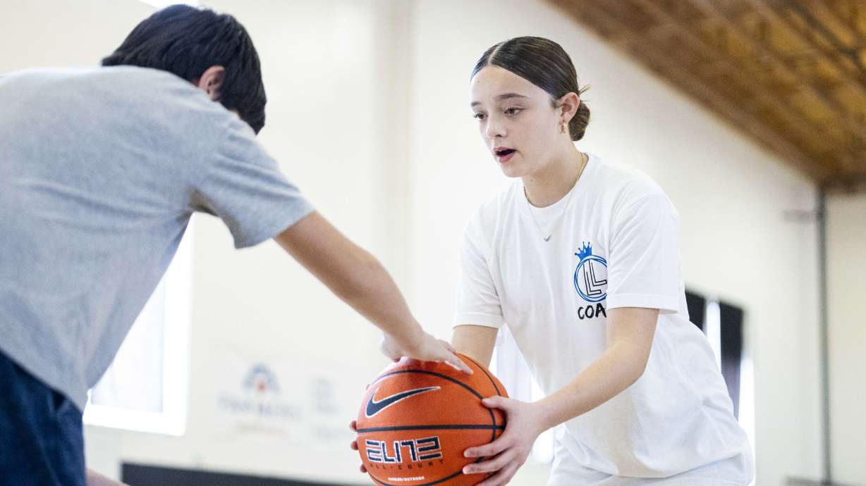 Liv Harness, 14, helps an attendee with a drill that requires dribbling a ball while tapping another ball during a basketball camp for children with Utah Foster Care and Raise The Future held at the Karl Malone Training Center in Lehi on Thursday.