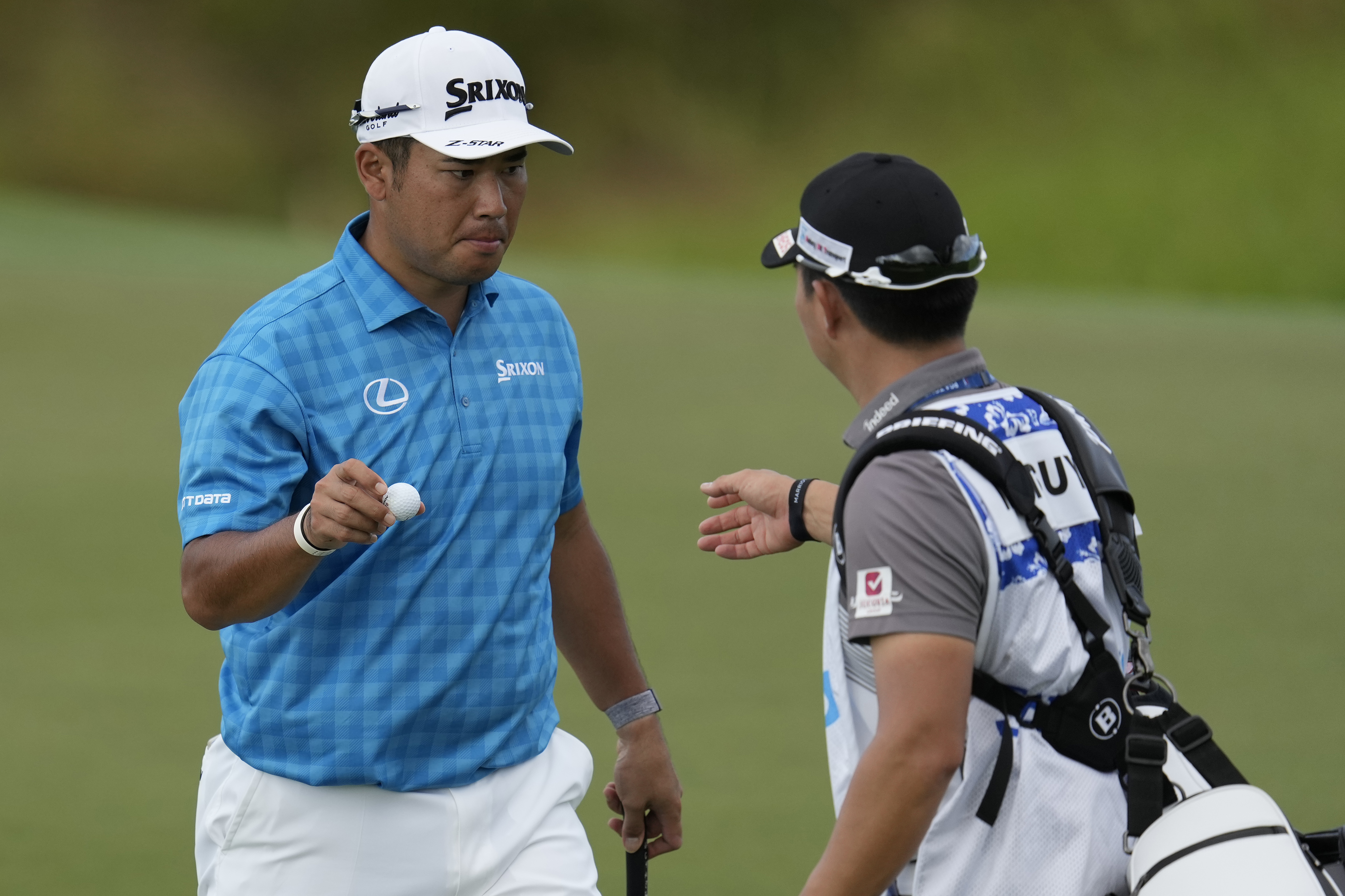 Hideki Matsuyama, of Japan,, left, hands his ball to his caddie on the 12th green during the first round of The Sentry golf event, Thursday, Jan. 2, 2025, at Kapalua Plantation Course in Kapalua, Hawaii.