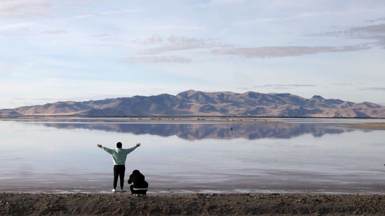 Zhenao Ji raises his arms while looking west from Stansbury Island towards the Lakeside mountain range as Swift Hu takes photos of him in Tooele County on Thursday. Great Salt Lake State Park in nearby Magna experienced another increase in visitation last year from people all over the world.