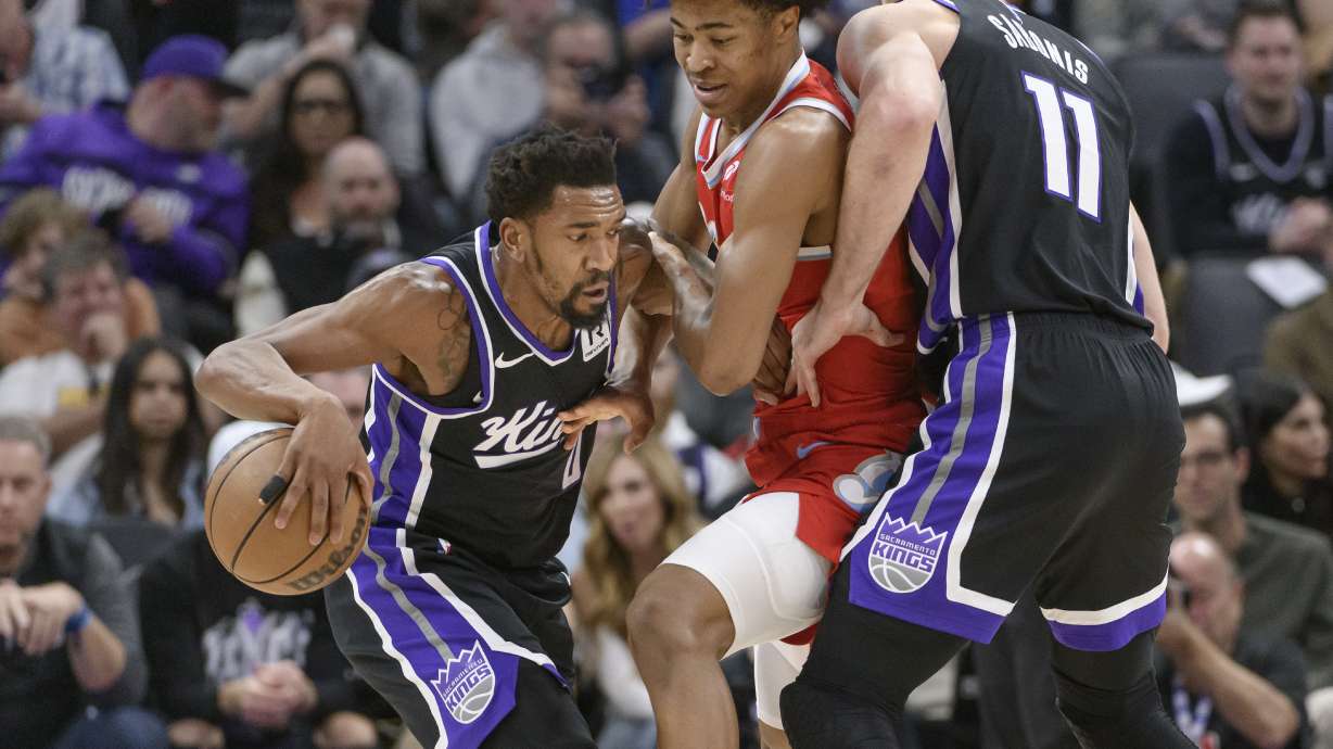 Sacramento Kings guard Malik Monk, left, drives past Memphis Grizzlies forward Jaylen Wells, center, during the first half of an NBA basketball game in Sacramento, Calif., Friday, Jan. 3, 2025.