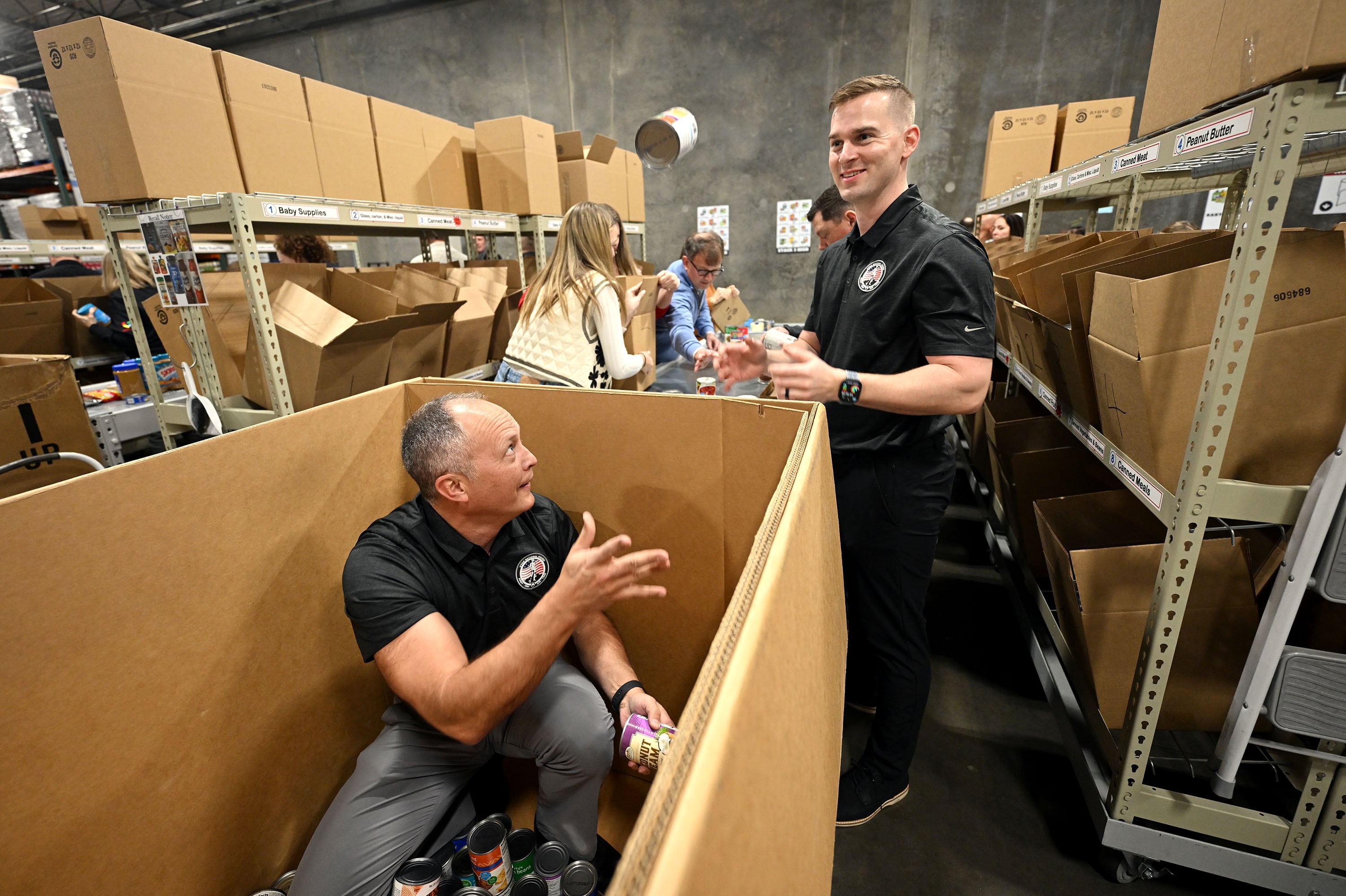 Maj. Gen. Daniel D. Boyack, adjutant general Utah National Guard, tosses a can of food to Quinton Jorgensen, aide de camp, as they join Gov. Spencer Cox, first lady Abby Cox, Lt. Gov. Deidre Henderson and other government employees at the Utah Food Bank to serve in Salt Lake City on Tuesday.