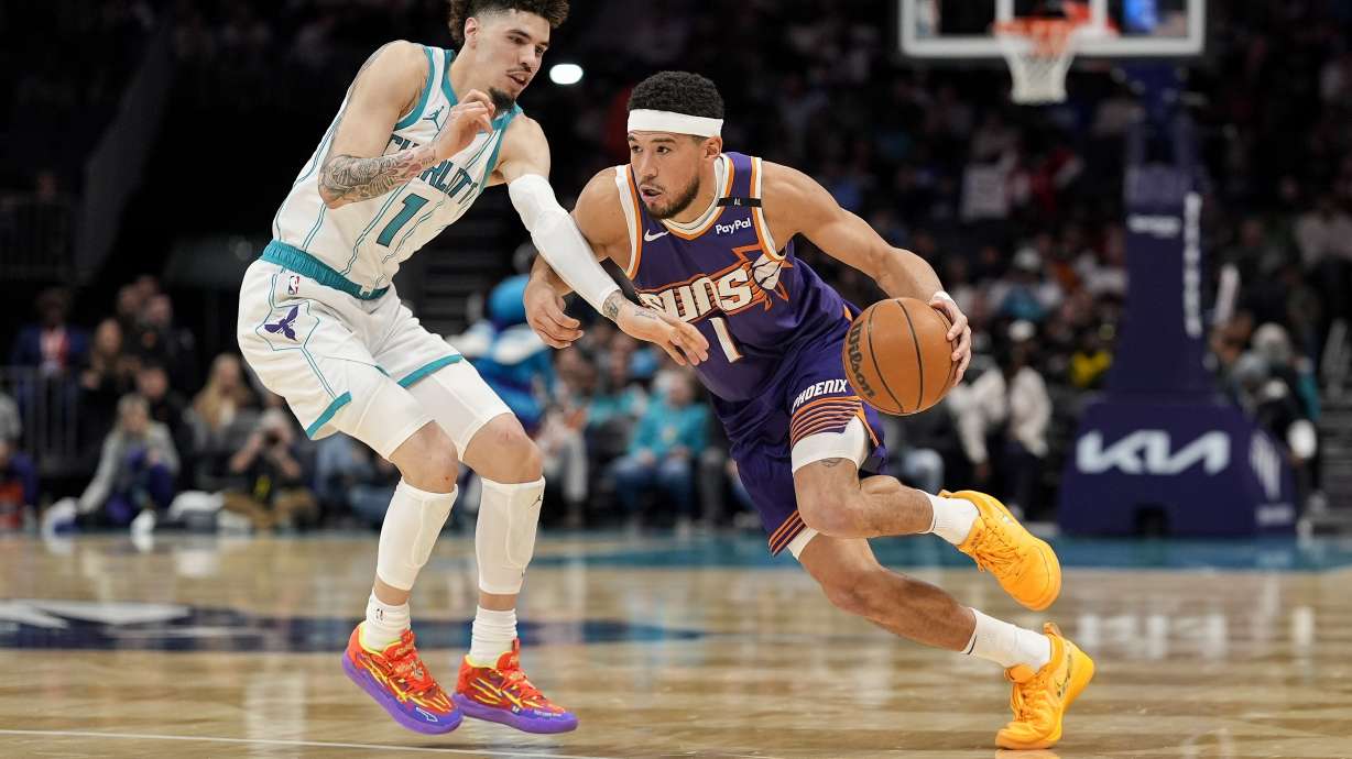 Phoenix Suns guard Devin Booker (1) drives to the basket against Charlotte Hornets guard LaMelo Ball (1) during the first half of an NBA basketball game in Charlotte, N.C., Tuesday, Jan. 7, 2025.