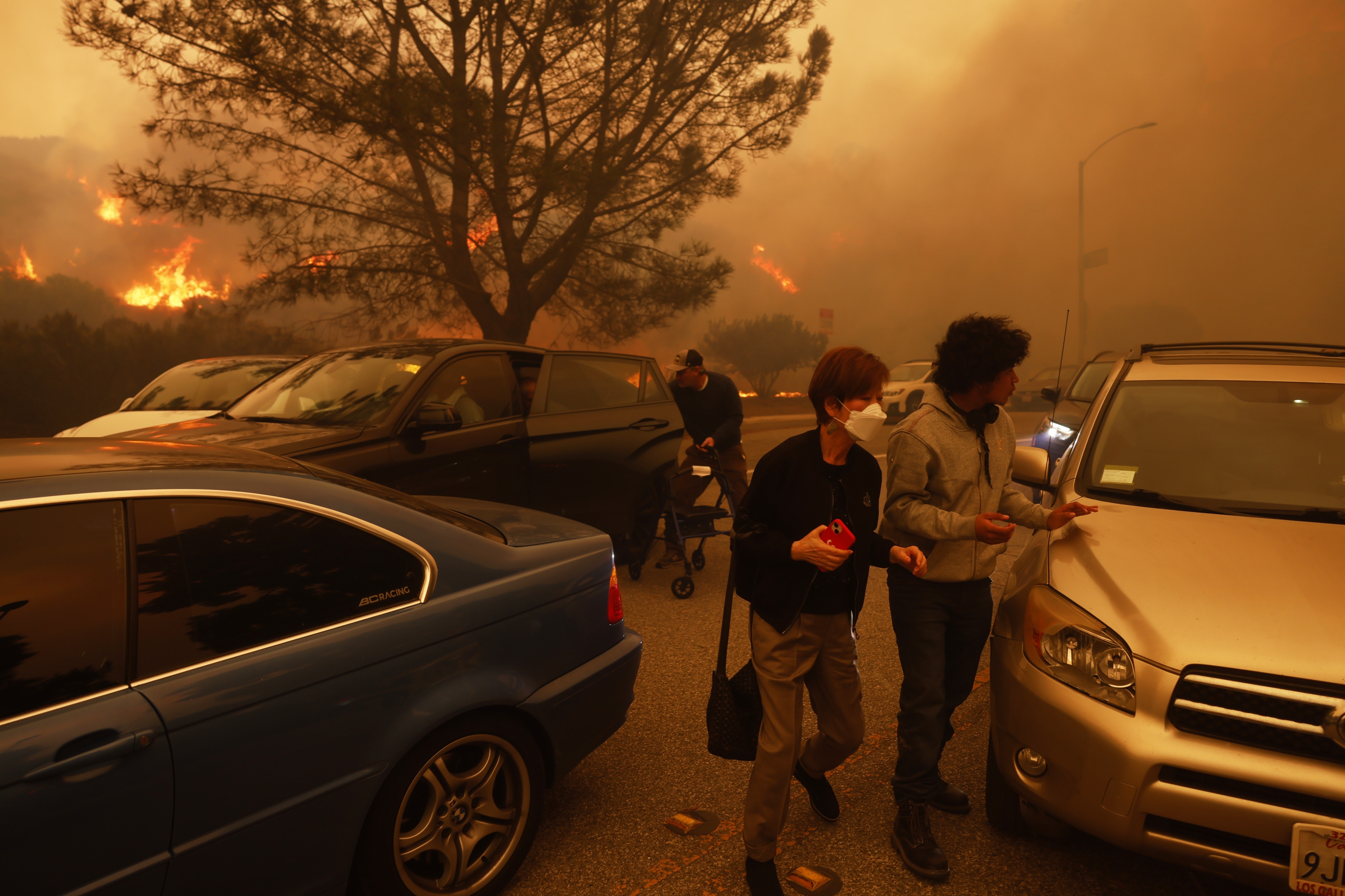 People flee from the advancing Palisades Fire, by car and on foot, in the Pacific Palisades neighborhood of Los Angeles Tuesday.