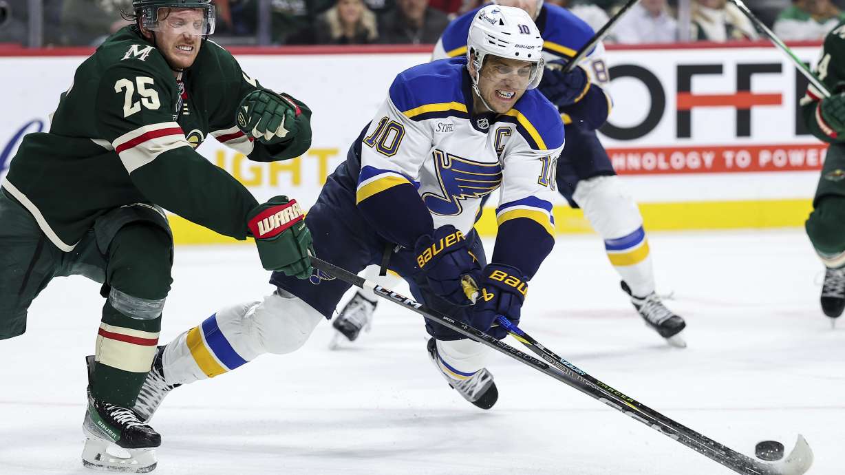 St. Louis Blues center Brayden Schenn, right, and Minnesota Wild defenseman Jonas Brodin reach for the puck during the third period of an NHL hockey game, Tuesday, Jan. 7, 2025, in St. Paul, Minn.
