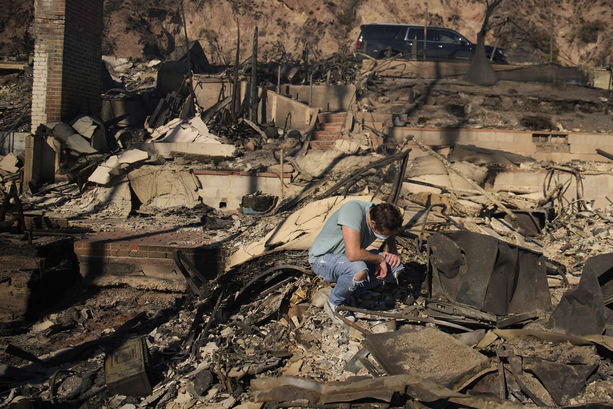 Luke Dexter kneels as he sifts through the remains of his father's fire-ravaged beachfront property in the aftermath of the Palisades Fire on Friday in Malibu, Calif.
