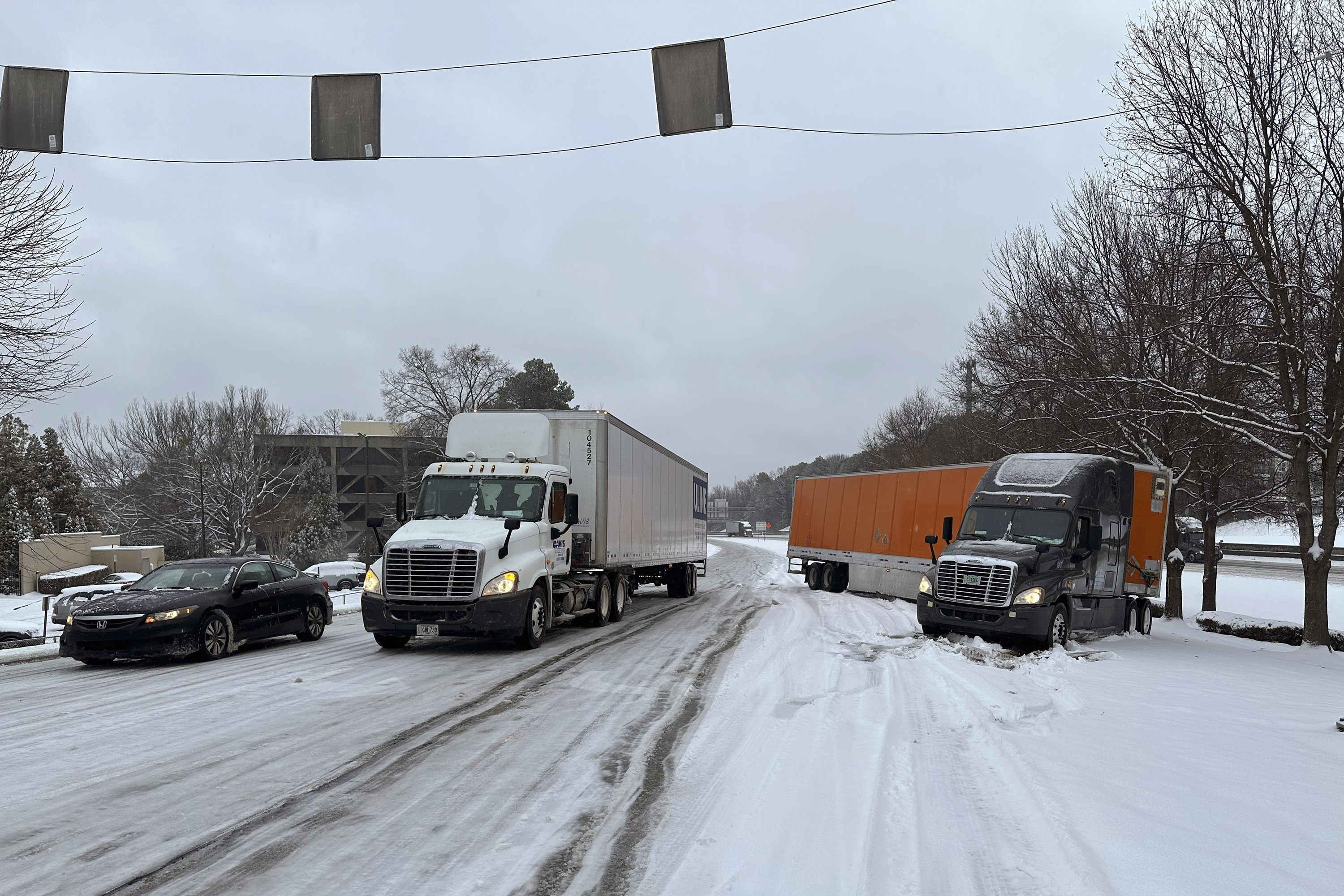 A truck is jackknifed as another spins its wheels on a slushy offramp off Interstate 285 northeast of downtown in Atlanta on Friday, Jan. 10, 2025.