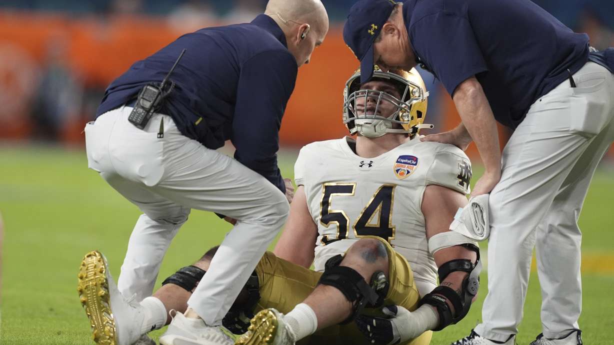 Notre Dame offensive lineman Anthonie Knapp (54) is assisted on the field during the first half of the Orange Bowl NCAA College Football Playoff semifinal game against Penn State, Thursday, Jan. 9, 2025, in Miami Gardens, Fla.