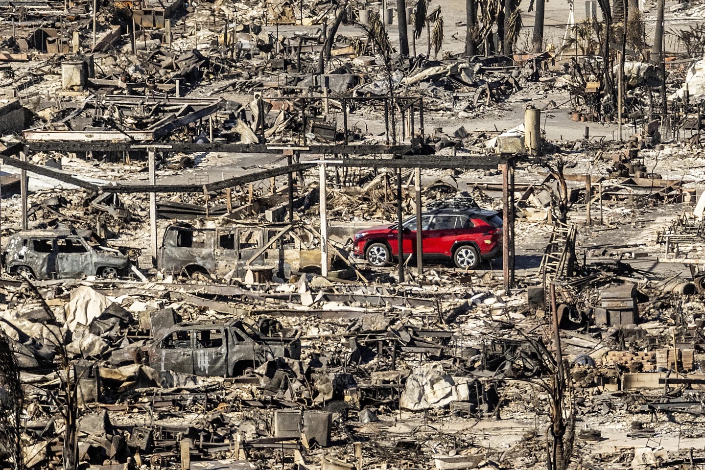 A car passes by homes and vehicles destroyed by the Palisades Fire at the Pacific Palisades Mobile Bowl Estates on Sunday in Los Angeles, Calif.