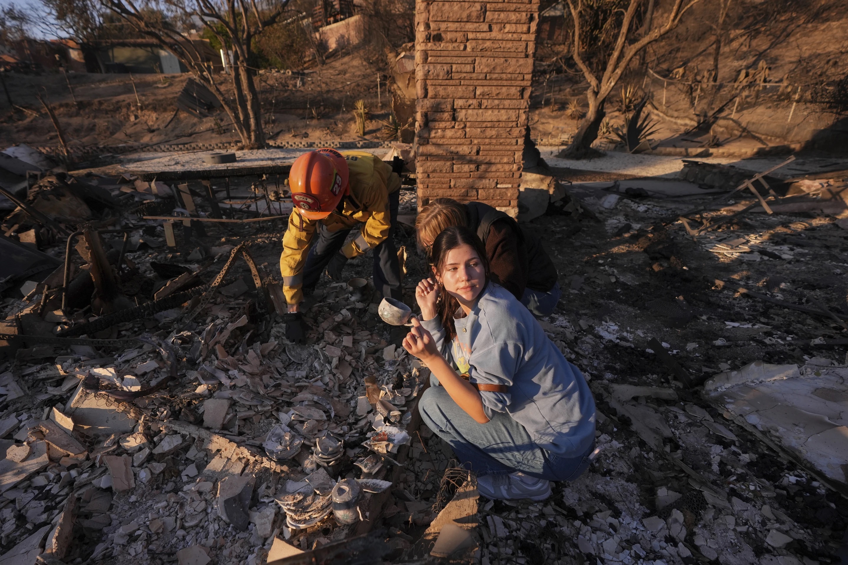 Ella Venne, front, holds a cup she found in the remains of her family's home destroyed by the Eaton Fire as she searches with Glendale Fire Department captain Chris Jernegan, left, and his wife Alison in Altadena, Calif., Saturday.