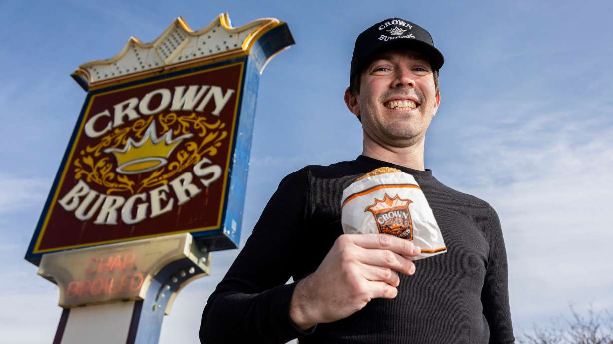 Bryant Heath poses in front of the Crown Burgers location at 118 N. 300 West in Salt Lake City with the namesake burger of the establishment, a Crown Burger, on Jan. 10.