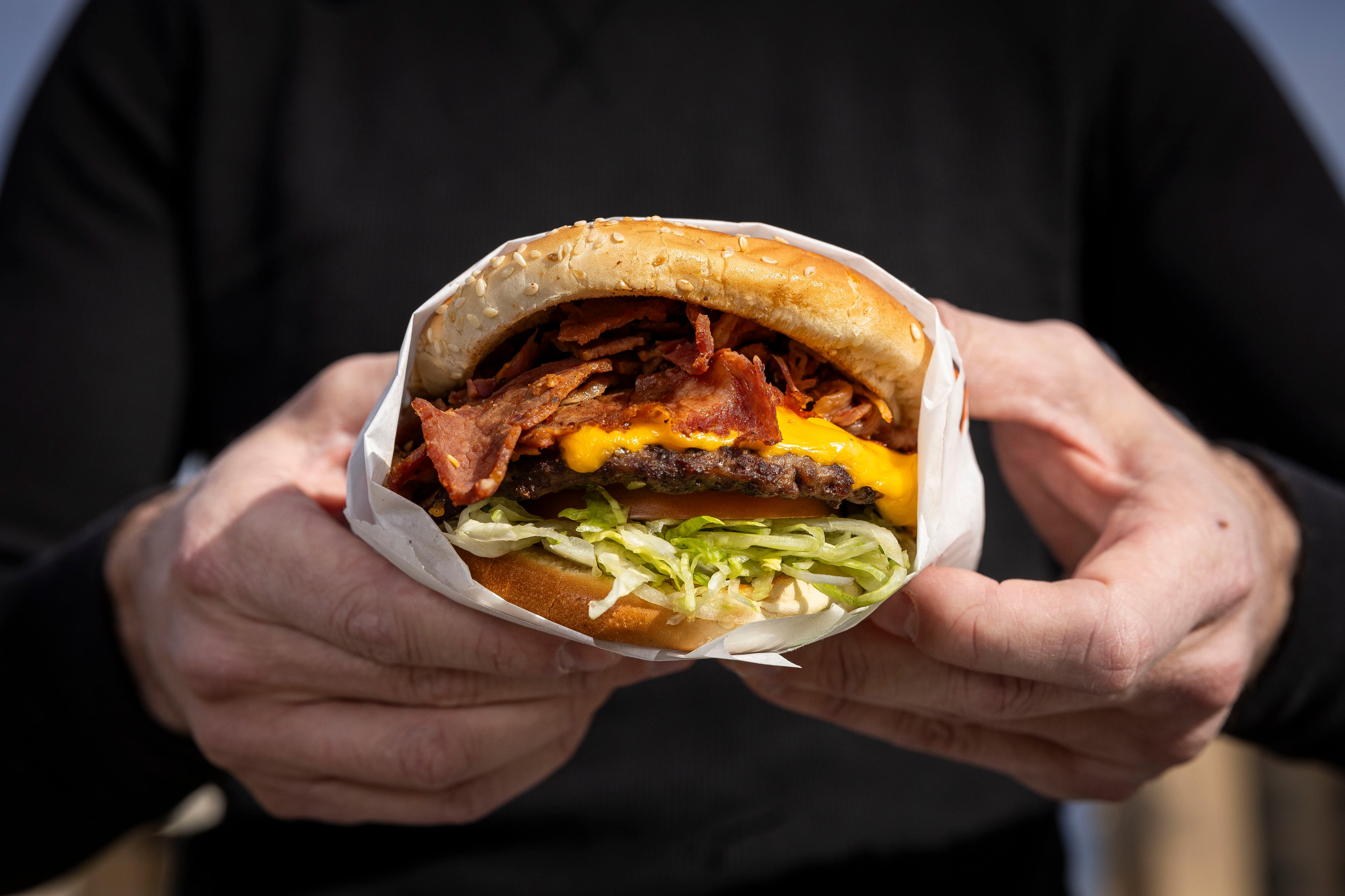 Bryant Heath poses in front of the Crown Burgers location at 118 N. 300 West in Salt Lake City with the namesake burger of the establishment, a Crown Burger, on Jan. 10.