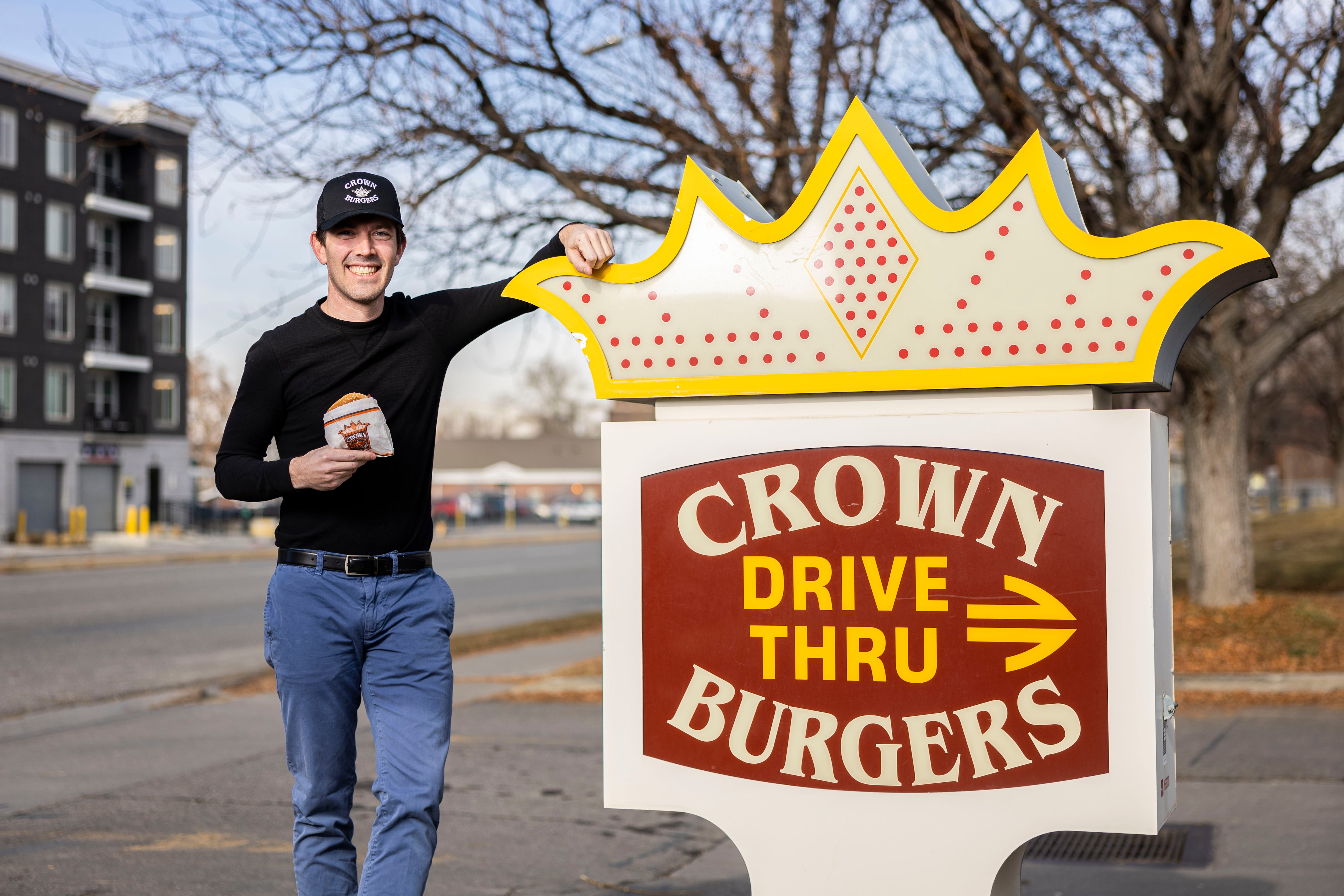 Bryant Heath poses in front of the Crown Burgers location at 118 N. 300 West in Salt Lake City with the namesake burger of the establishment, a Crown Burger, on Jan. 10. Heath went to all eight Crown Burgers locations in one day on Dec. 23, 2024.