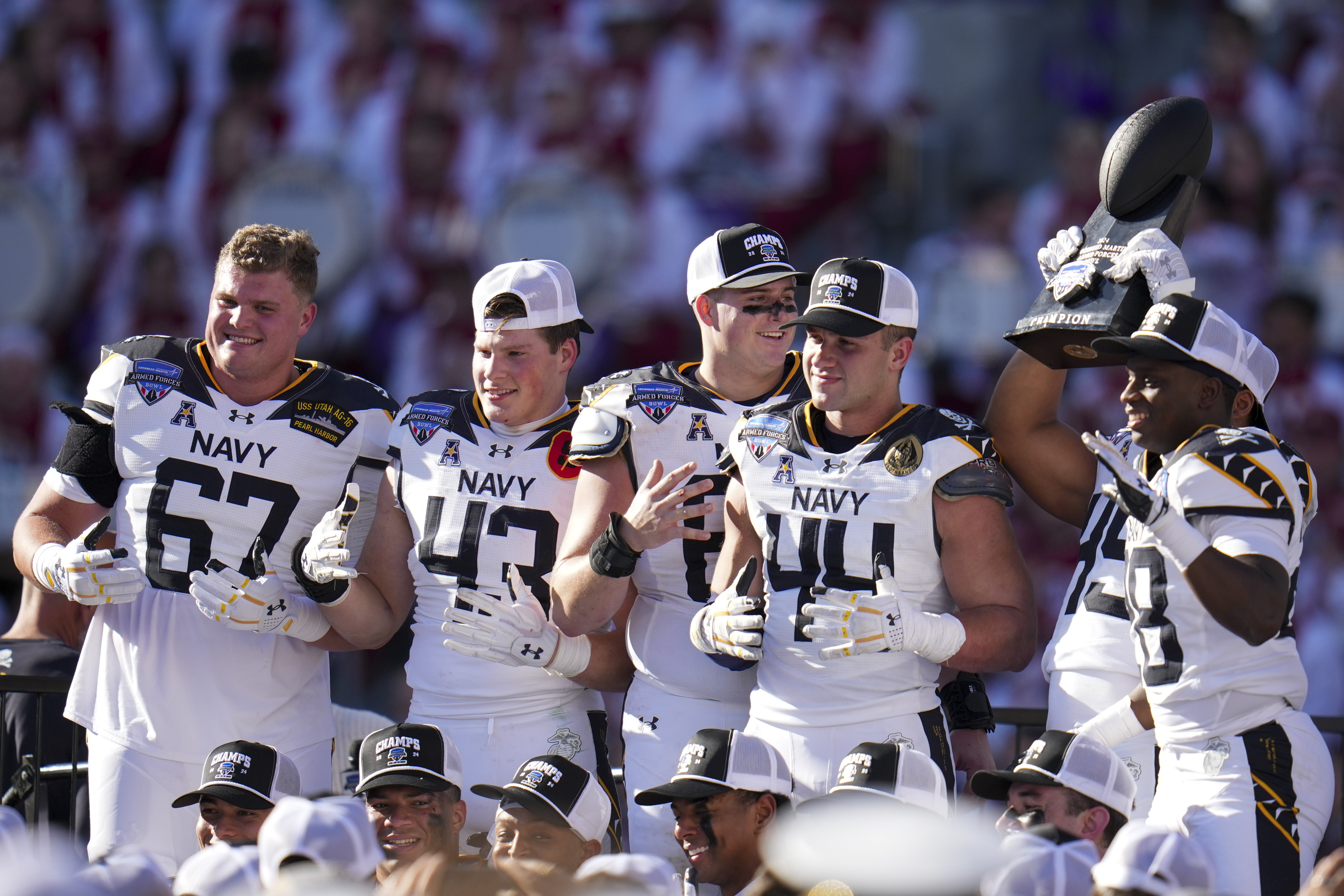 Navy players pose with the Lockheed Martin Armed Forces Bowl trophy following the Armed Forces Bowl NCAA college football game against Oklahoma, Friday, Dec. 27, 2024, in Fort Worth, Texas. Navy won 21-20.