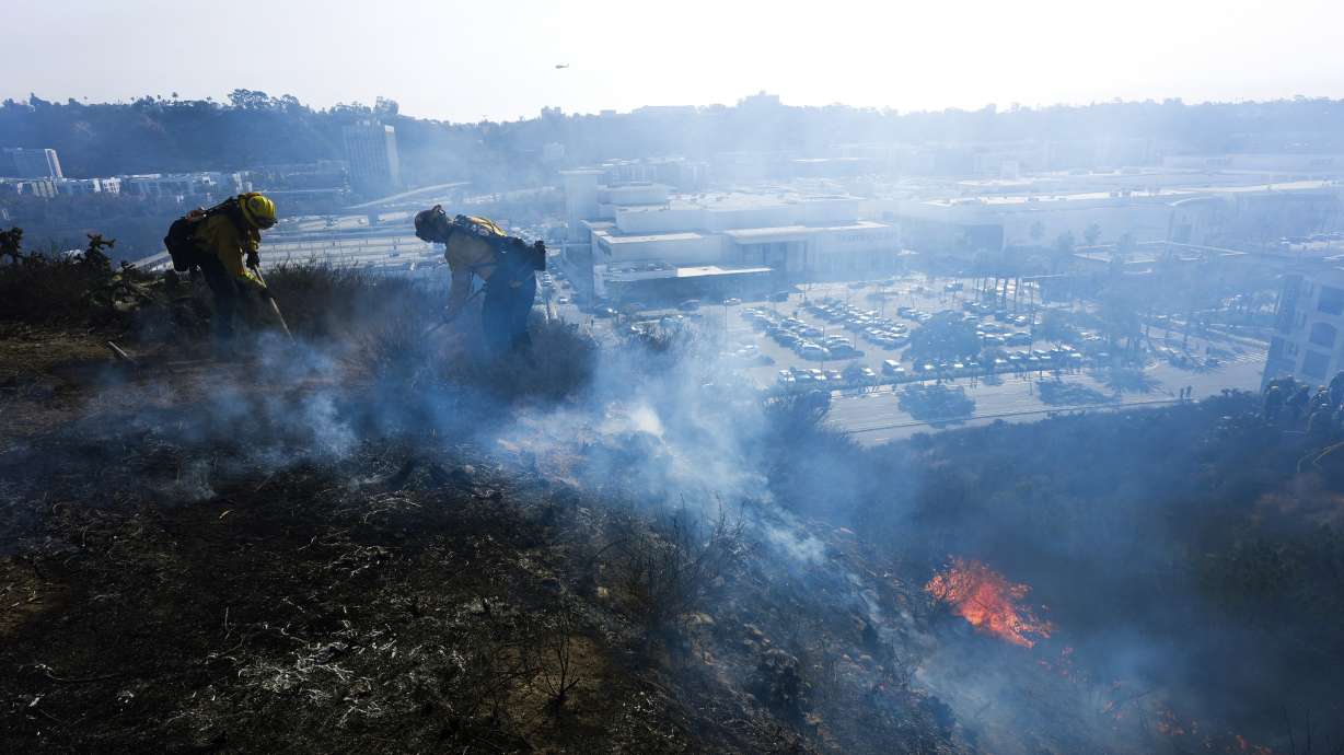 San Diego firefighters knock down a small brush along a hillside over the Mission Valley Shopping Mall in San Diego on Tuesday. The Hughes Fire broke out late Wednesday morning and quickly burned through hundreds of acres of trees and brush, sending up a huge plume of dark smoke near the Lake Castaic area.