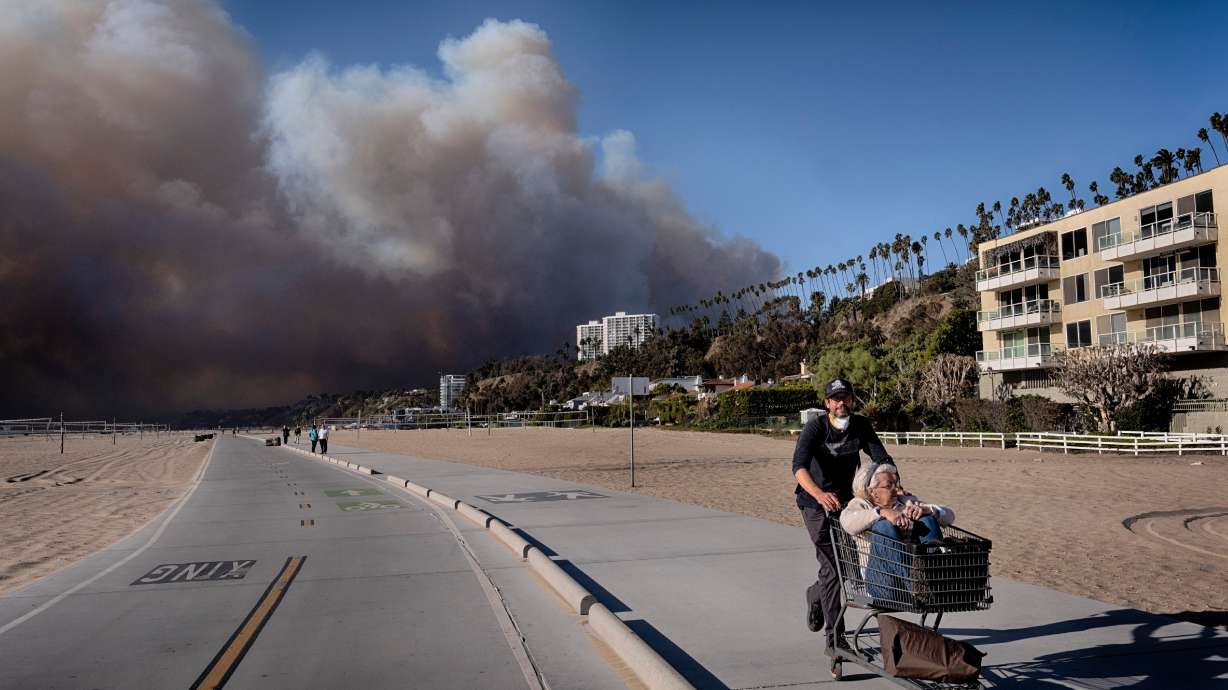 Jerome Krausse pushes his mother-in-law in a shopping cart as they evacuate from their home in the Pacific Palisades after a wildfire swept through their neighborhood in Santa Monica, Calif., on Jan. 7. More Californians may be moving to Utah.