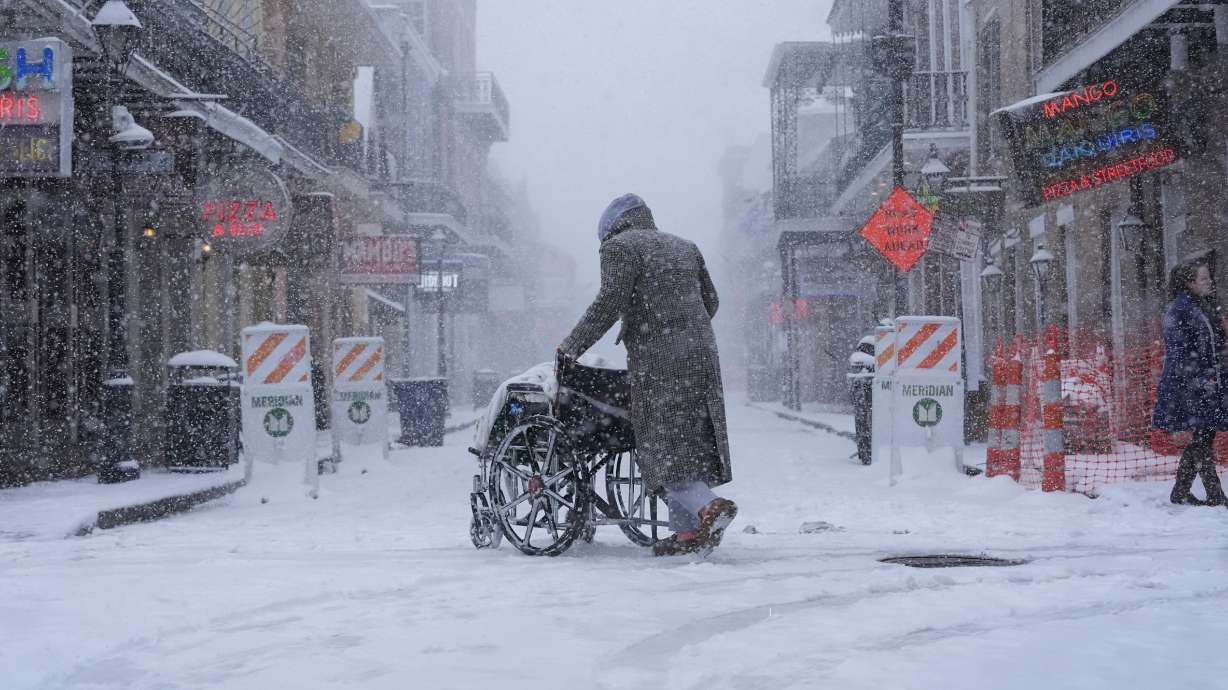 A person pushes a wheelchair across Bourbon Street as snow falls in the French Quarter in New Orleans, Tuesday.