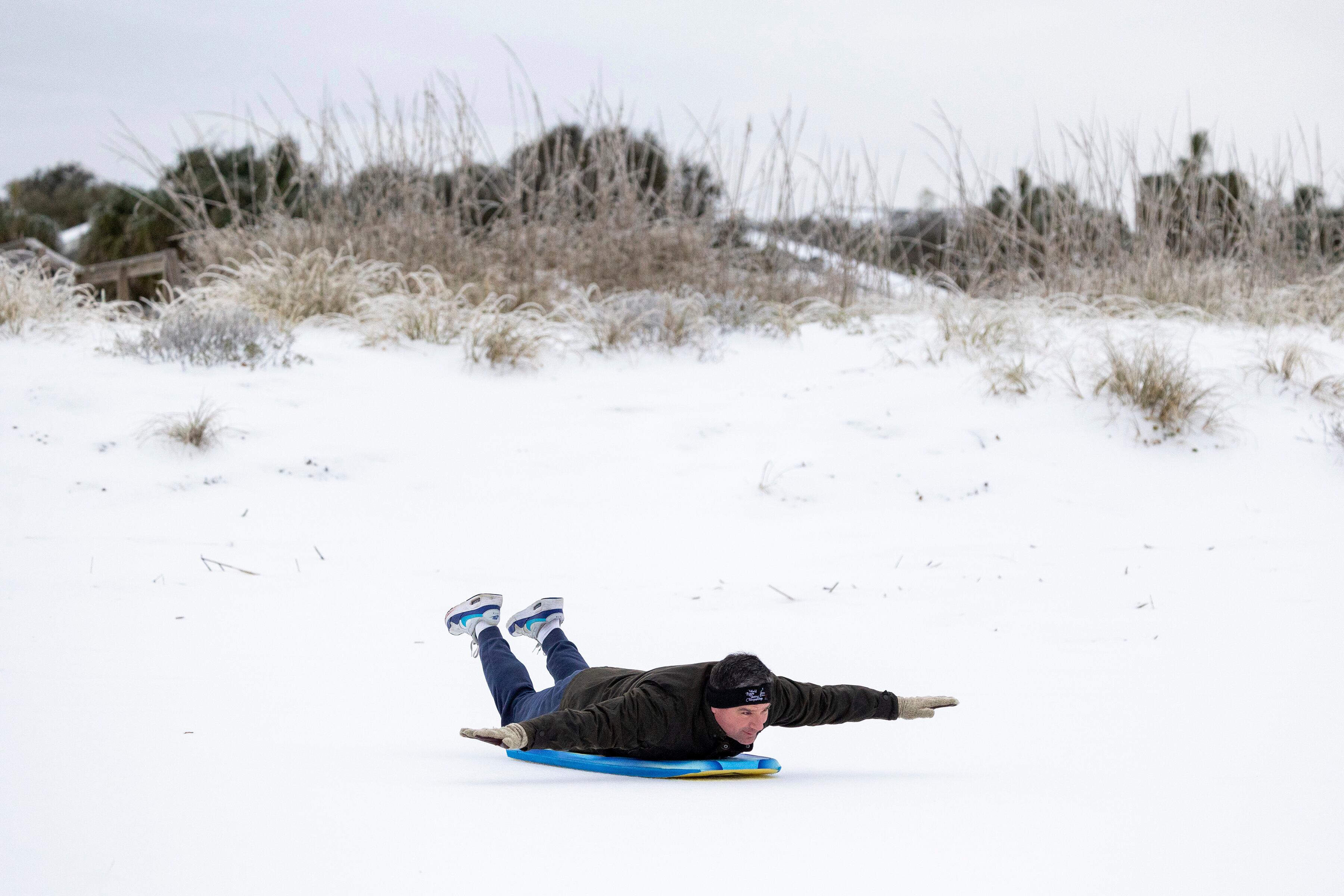 Alex Spiotta, from the Isle of Palms, S.C., uses a boogie board to sled across the beach after a winter storm dropped ice and snow Wednesday, on the Isle of Palms, S.C.