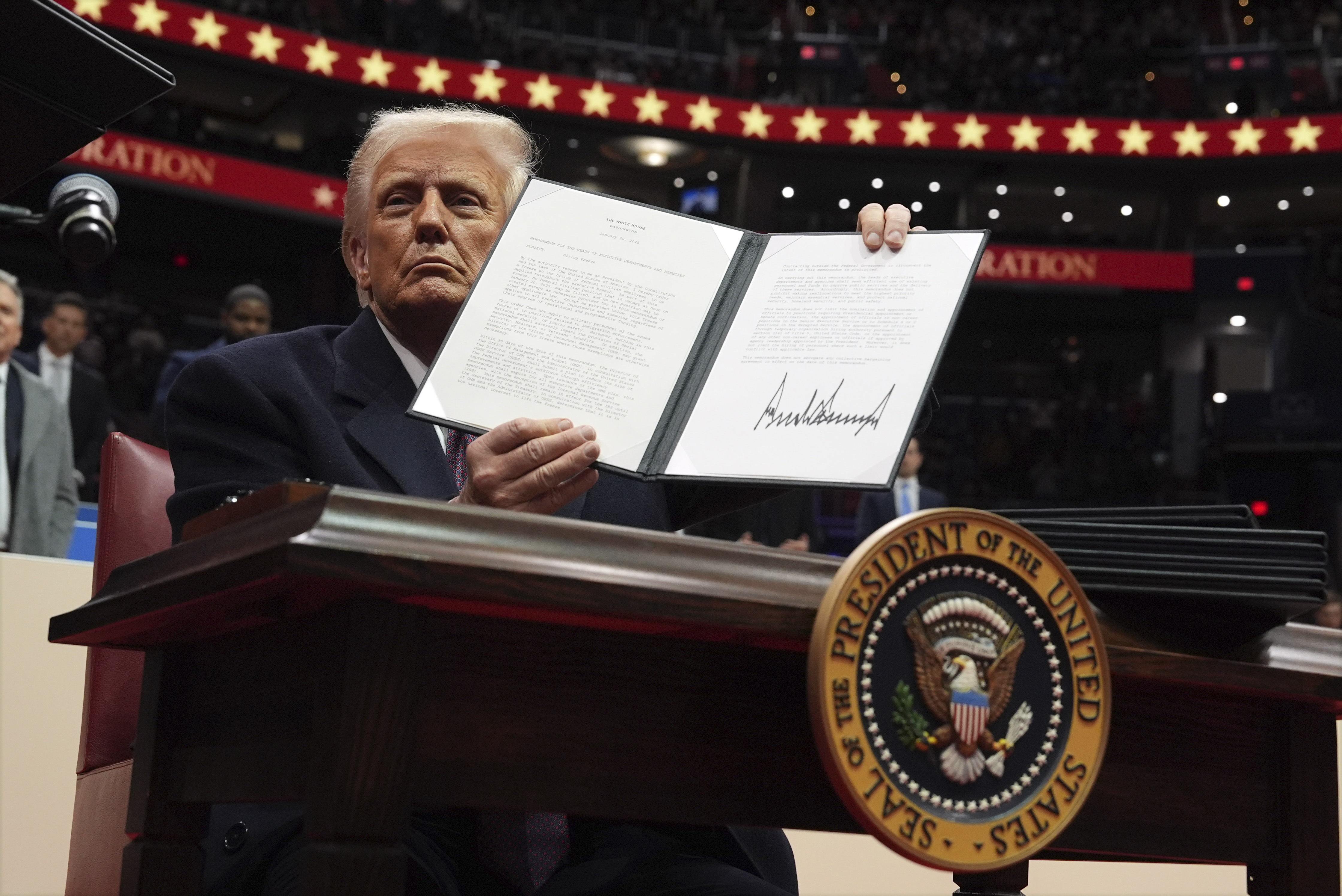 President Donald Trump signs an executive order as he attends an indoor Presidential Inauguration parade event at Capital One Arena, Monday, in Washington.