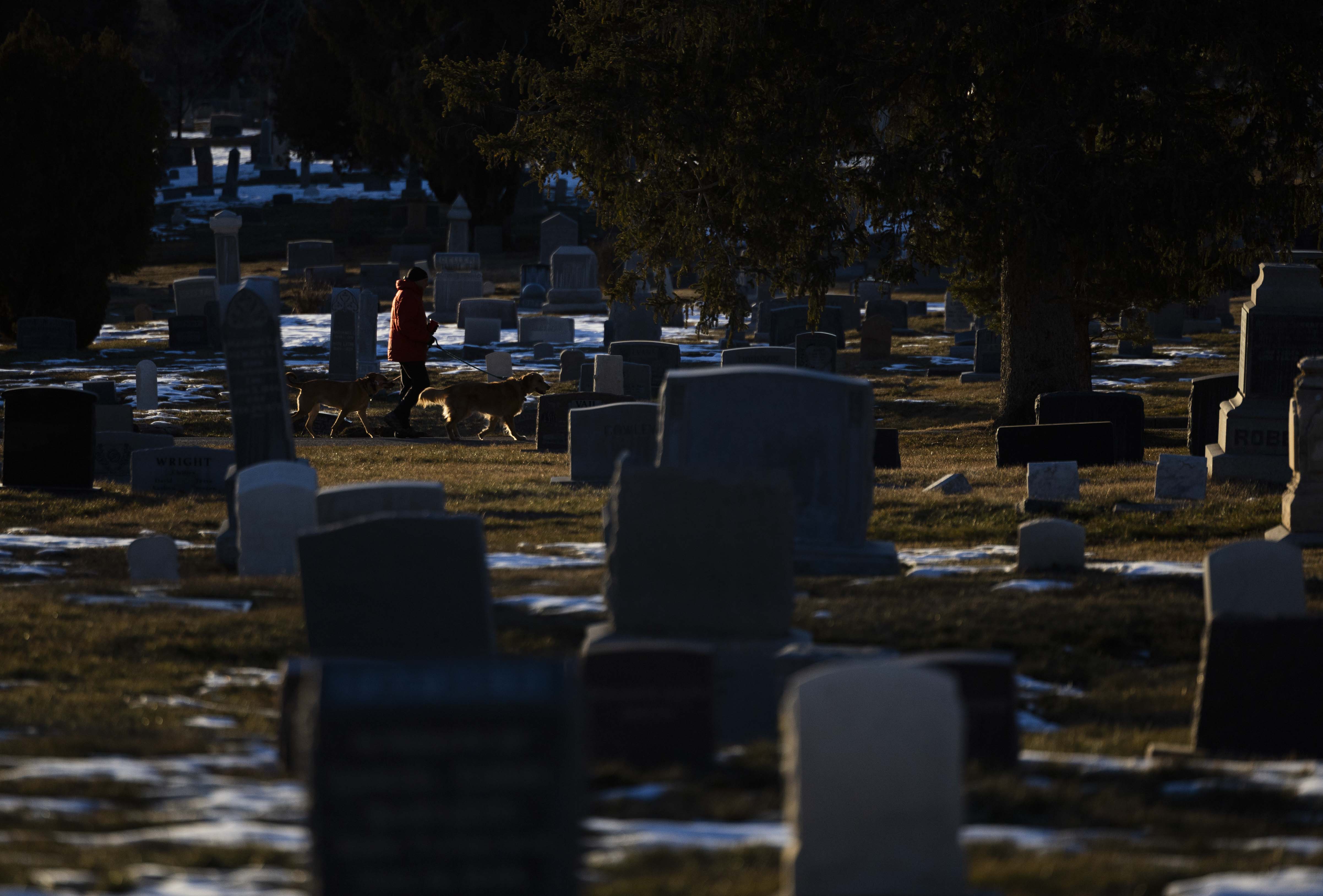 A person can be seen through rows of gravestones walking their dogs in the Salt Lake City Cemetery in Salt Lake City on Wednesday.