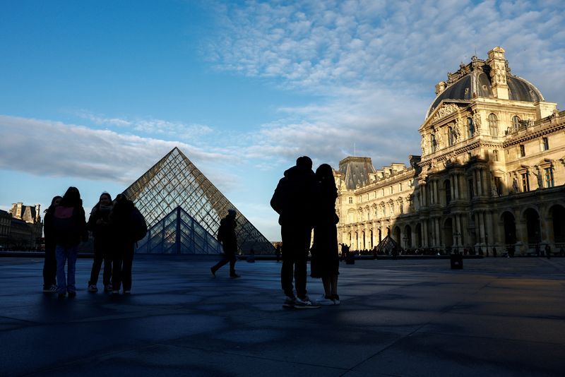 Tourists walk past the glass Pyramid entrance of the Louvre Museum in Paris, France, Thursday.