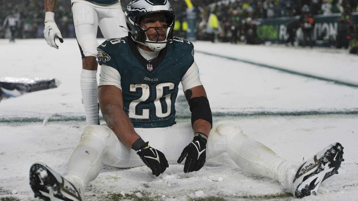 Philadelphia Eagles running back Saquon Barkley (26) sits in the snow as he celebrates his touchdown during the second half of an NFL football NFC divisional playoff game against the Los Angeles Rams on Sunday, Jan. 19, 2025, in Philadelphia.