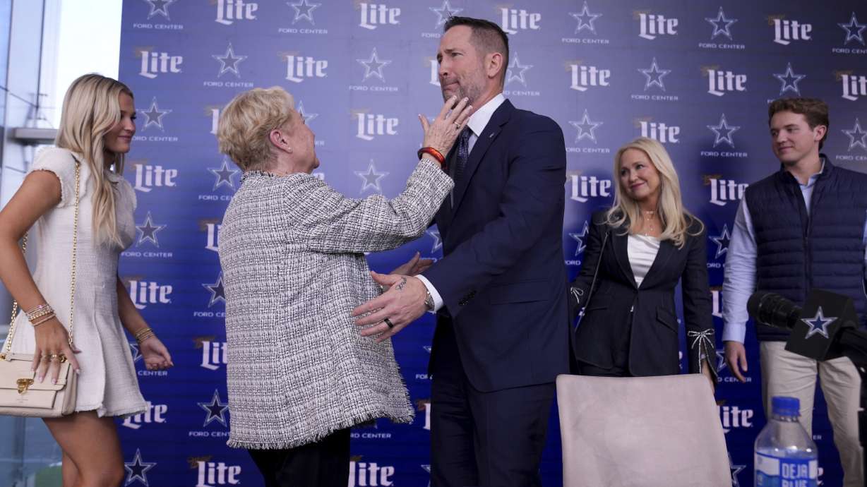 Dallas Cowboys new head coach Brian Schottenheimer, center right, becomes emotional as he reaches to hug his mother, Pat Schottenheimer, center left as his daughter, Savannah, from left rear, wife Gemmi and son Sutton, right rear, look on after a news conference where at the team's headquarters in Frisco, Texas, Monday, Jan. 27, 2025.