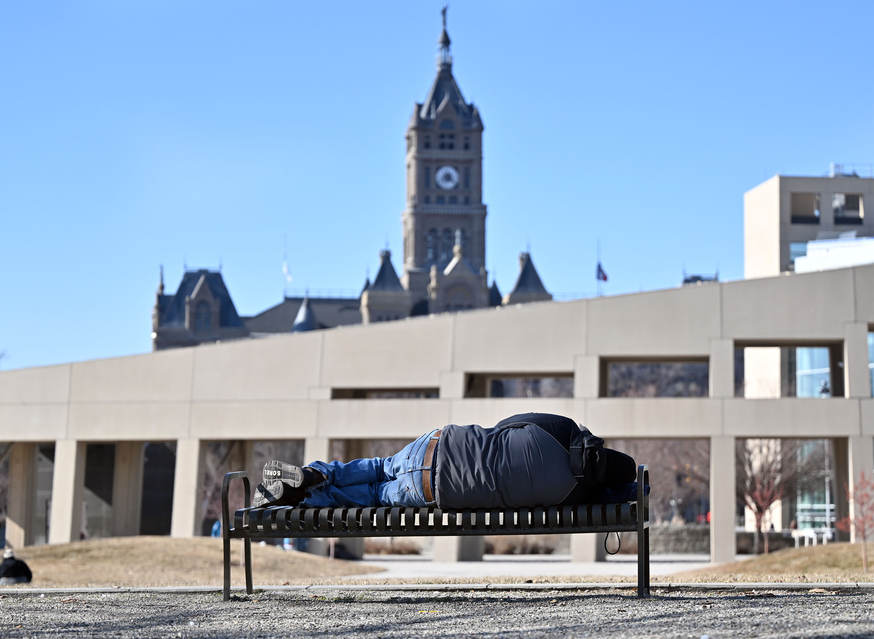 A person lays on a bench near the Salt Lake City Police department and library in Salt Lake City on Tuesday. Salt Lake City Mayor Erin Mendenhall said Tuesday that public safety, homelessness and affordable housing are "urgent" issues the city plans to tackle this year.