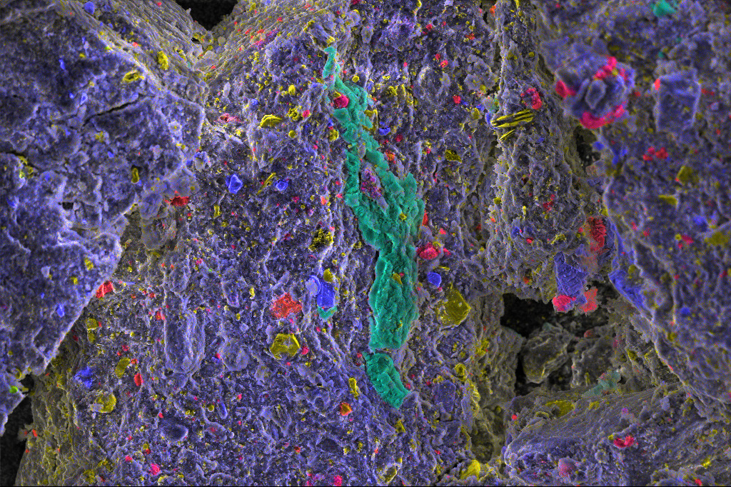 This image is an energy-dispersive spectrometric map of an unprepared grain of asteroid Bennu. Phosphorus is shown in green, calcium in red, iron in yellow and magnesium in blue. Researchers identify 0.1 mm vein magnesium sodium phosphate (green cluster in the center) formed by evaporation. They hypotetize that phosphate may have played a role in the formation of organic molecules found in the samples.