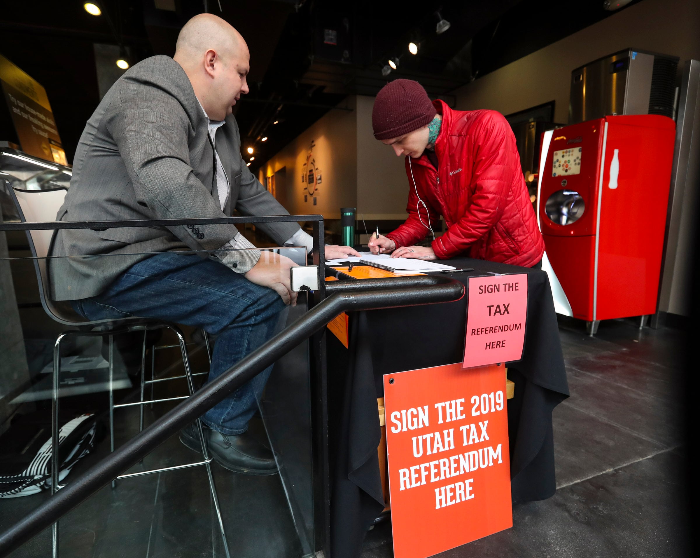 Kyle Green, left, a volunteer coordinator for a citizens referendum aimed at repealing a tax reform package passed by the Legislature in December, explains the issue to Carlin Miner as he adds his name to the referendum inside the Harmons City Creek store in Salt Lake City on Jan. 16, 2020.