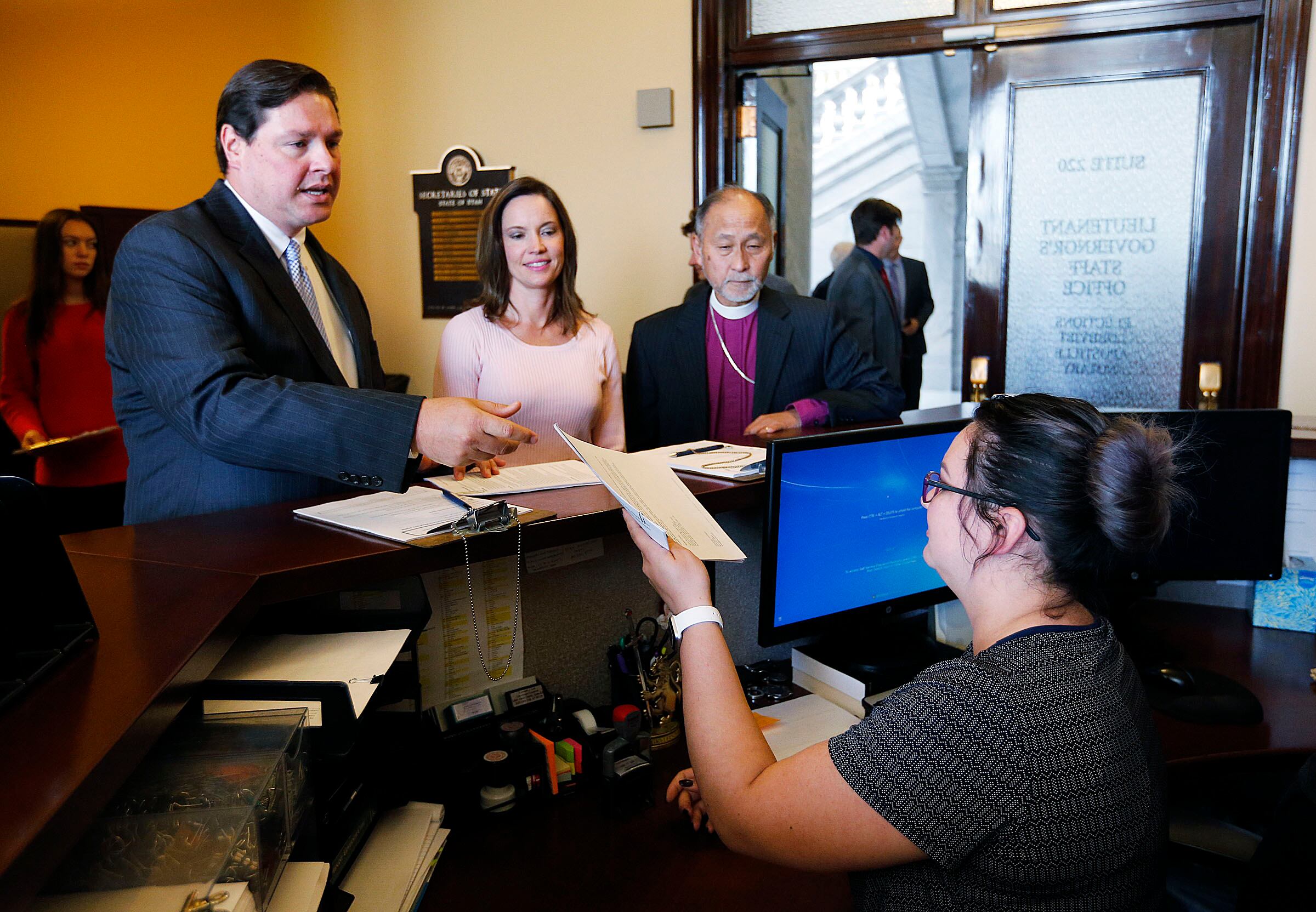 Alan Ormsby, left, of AARP Utah, Karina Andelin Brown and the Right Rev. Scott B. Hayashi, bishop of the Episcopal Diocese of Utah, deliver the Utah Decides Healthcare ballot proposal to Thais Stewart, a receptionist in the Utah Lieutenant Governor's Office, at the Capitol in Salt Lake City on Oct. 2, 2017.