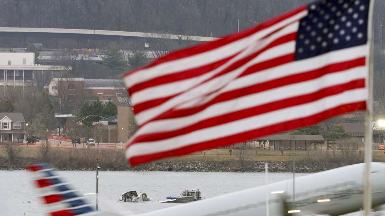 Search efforts are seen around a wreckage site of a deadly midair collision between an American Airlines jet and an Army helicopter, in the Potomac River near Ronald Reagan Washington National Airport, Friday, in Arlington, Va., as an American Airlines jet lifts off from the airport, foreground.