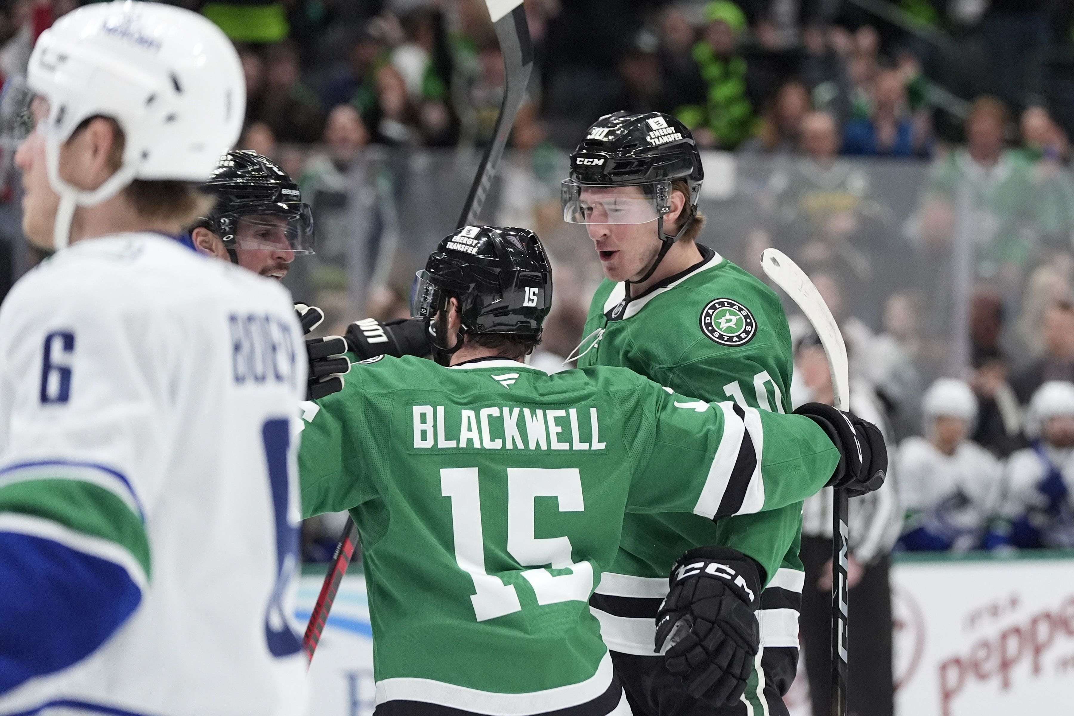 Dallas Stars center Oskar Bäck (10) celebrates his goal with teammates Colin Blackwell (15) and Brendan Smith as Vancouver Canucks right wing Brock Boeser (6) skates by during the first period of an NHL hockey game Friday, Jan. 31, 2025, in Dallas. 