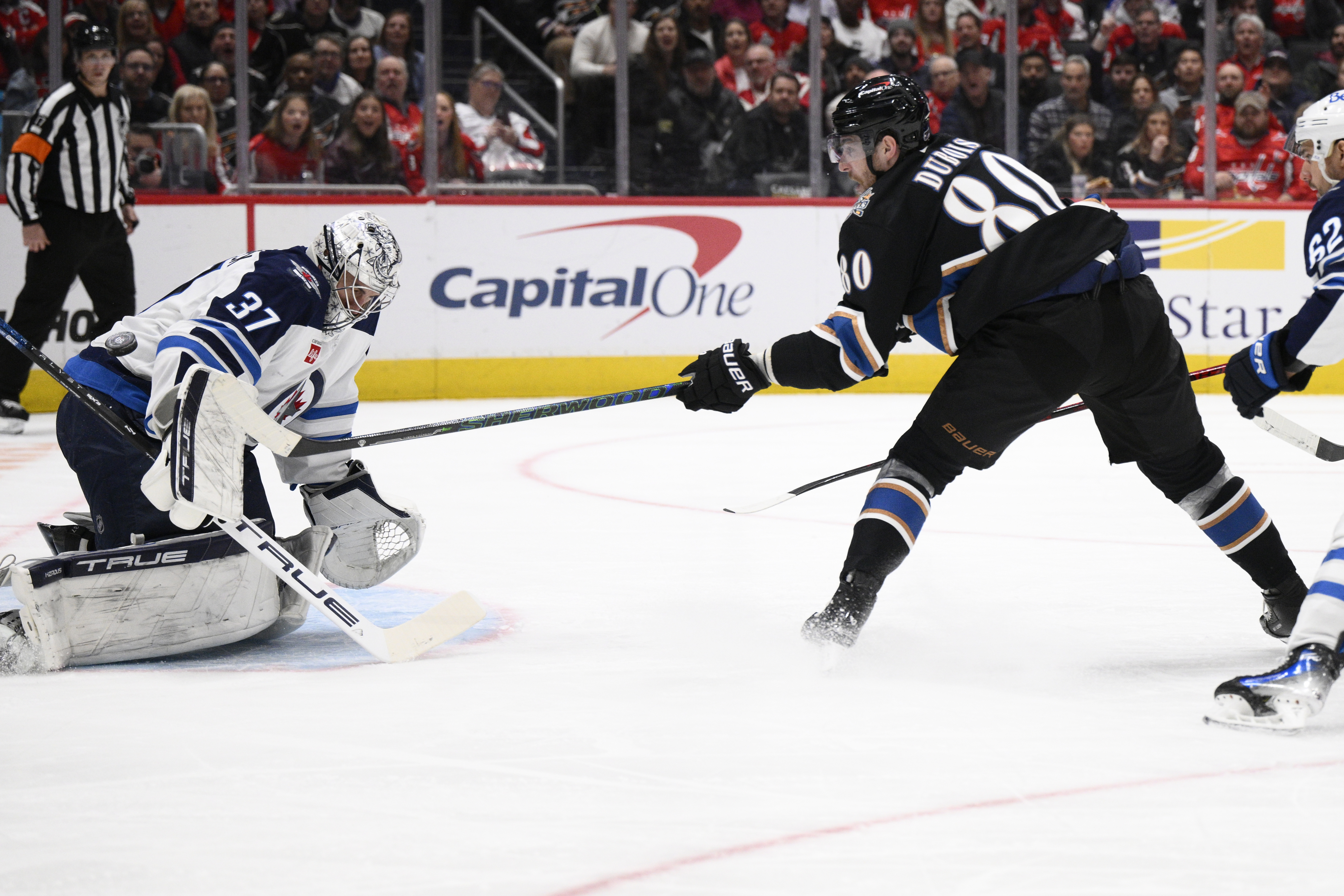 Washington Capitals left wing Pierre-Luc Dubois (80) tries to get the puck past Winnipeg Jets goaltender Connor Hellebuyck (37) during the first period of an NHL hockey game, Saturday, Feb. 1, 2025, in Washington. 