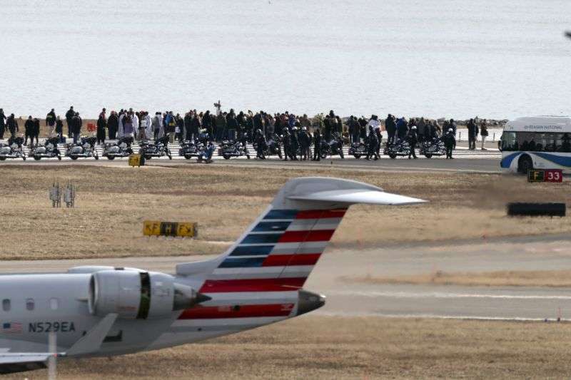 An American Airlines jet passes as family members of the victims of a mid-air collision between an American Airlines jet and an Army helicopter stand at the end of runway 33 near the wreckage site in the Potomac River at Ronald Reagan Washington National Airport, Sunday, in Arlington, Va.