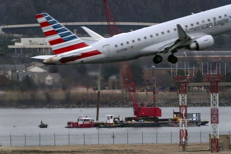 An American Eagle jet passes as rescue and salvage crews work near the wreckage of an American Airlines jet in the Potomac River from Ronald Reagan Washington National Airport, Sunday in Arlington, Va.