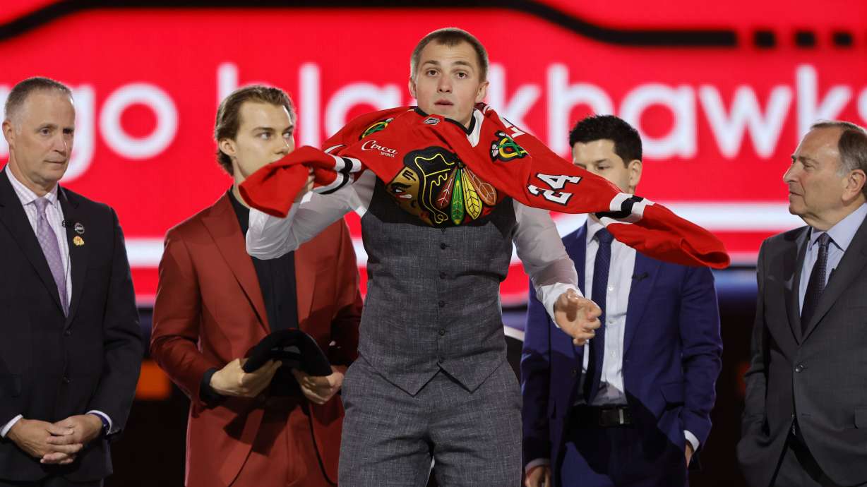 FILE - Artyom Levshunov, center, puts on a jersey after being selected by the Chicago Blackhawks during the first round of the NHL hockey draft, June 28, 2024, in Las Vegas.