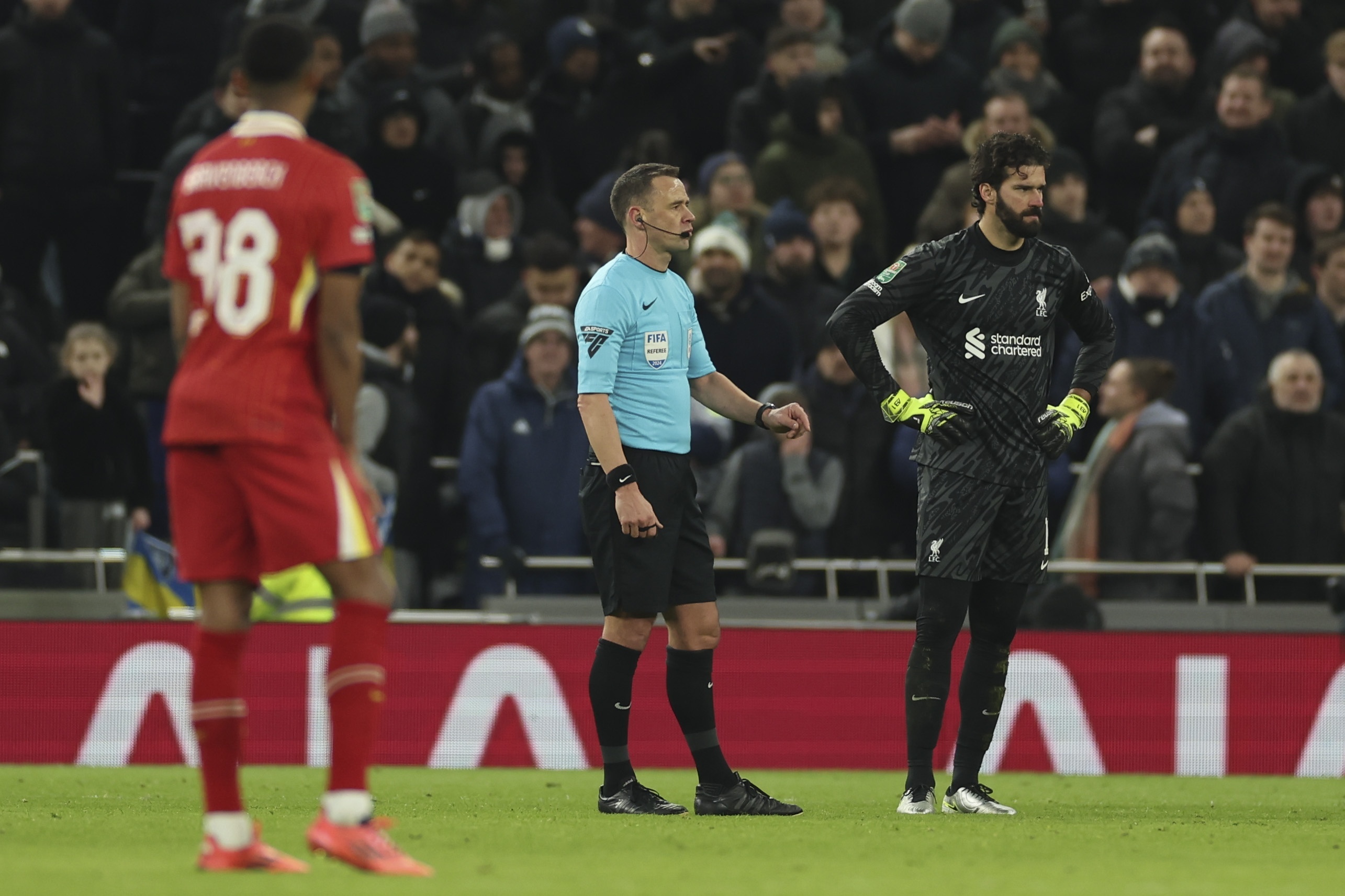 Referee Stuart Attwell stands alongside Liverpool's goalkeeper Alisson during the English League Cup semi final first leg soccer match between Tottenham and Liverpool, at the Tottenham Hotspur Stadium in London, Wednesday, Jan. 8, 2025.
