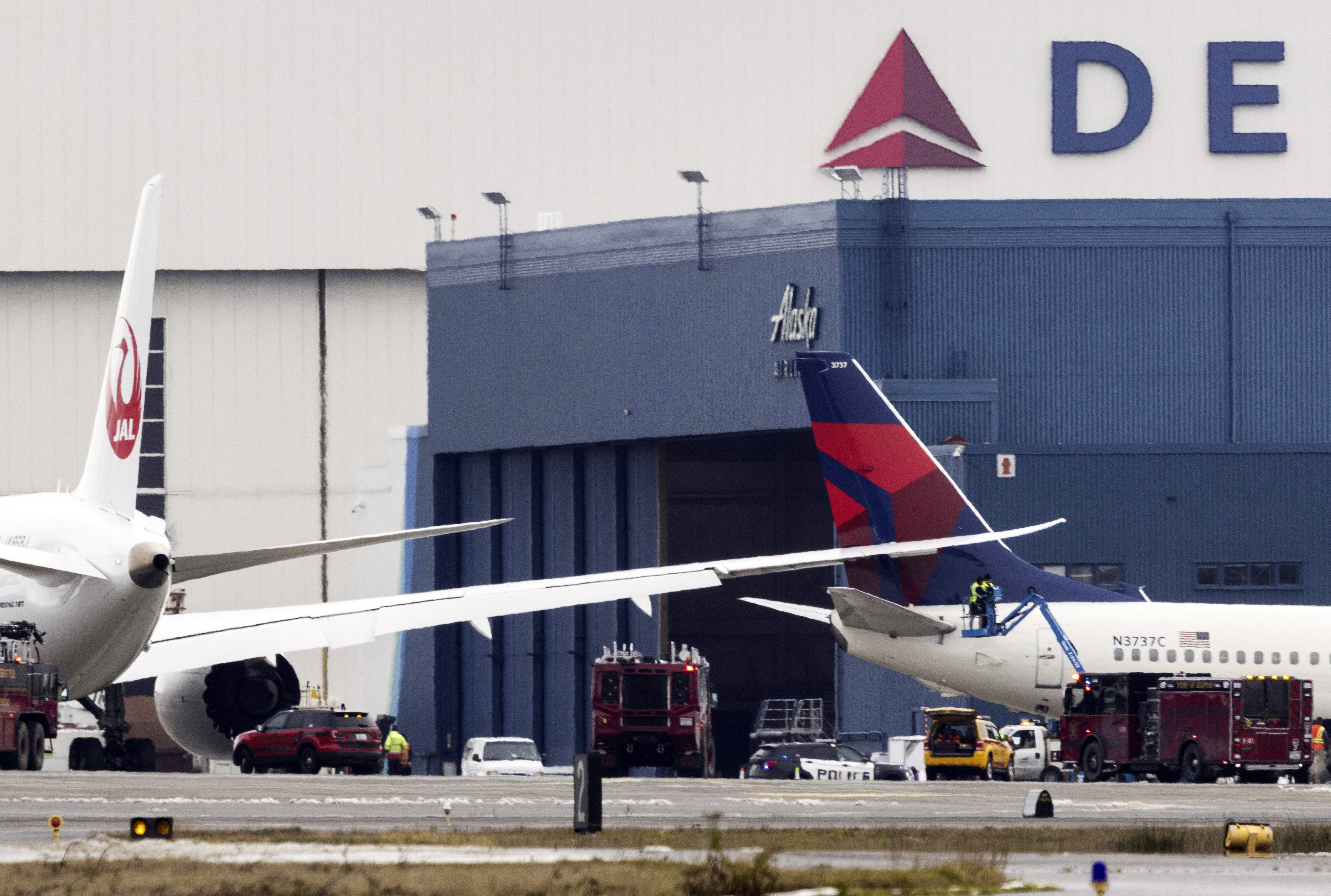 Workers on a lift check the area where the wing of a Japan Airlines jet went into the tail of a Delta Air Lines jet at the south end of a runway at Seattle-Tacoma International Airport on Wednesday.