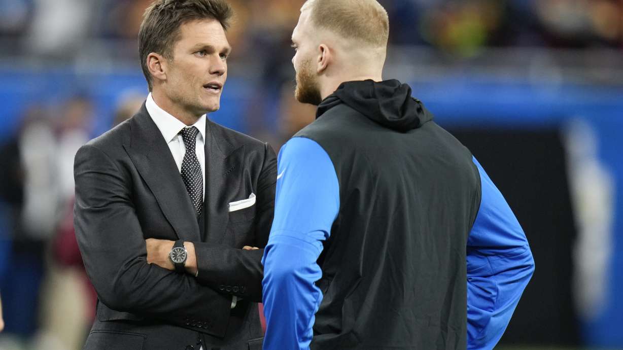 Tom Brady, left, talks with Detroit Lions defensive end Aidan Hutchinson before an NFL football divisional playoff game against the Washington Commanders, Saturday, Jan. 18, 2025, in Detroit.