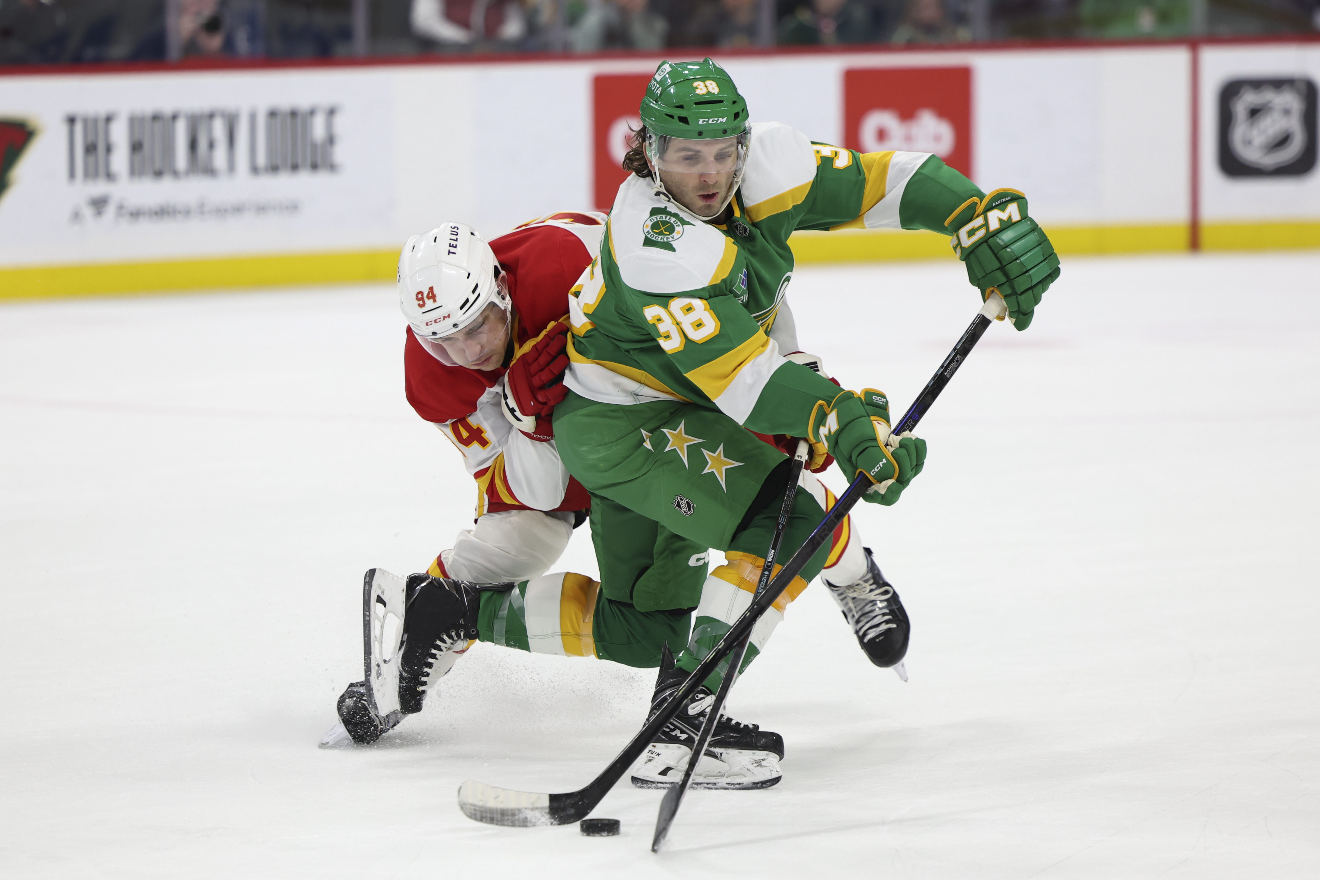 Calgary Flames defenseman Brayden Pachal and Minnesota Wild right wing Ryan Hartman (38) battle for the puck during the third period of an NHL hockey game, Saturday, Jan. 25, 2025, in St. Paul, Minn.