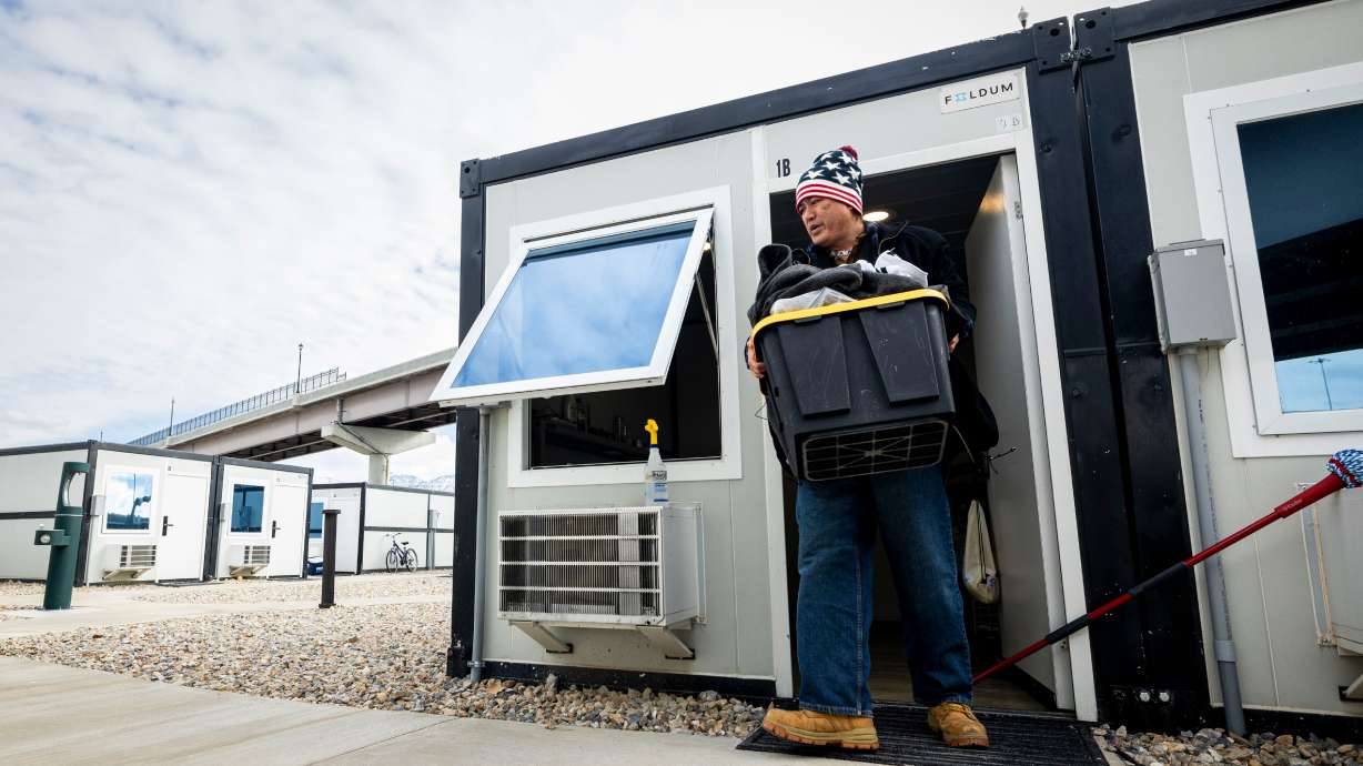 Dixie Nennis moves belongings outside of his microshelter unit so that he can mop the floor at a microshelter community operated by Switchpoint in Salt Lake City on Thursday.
