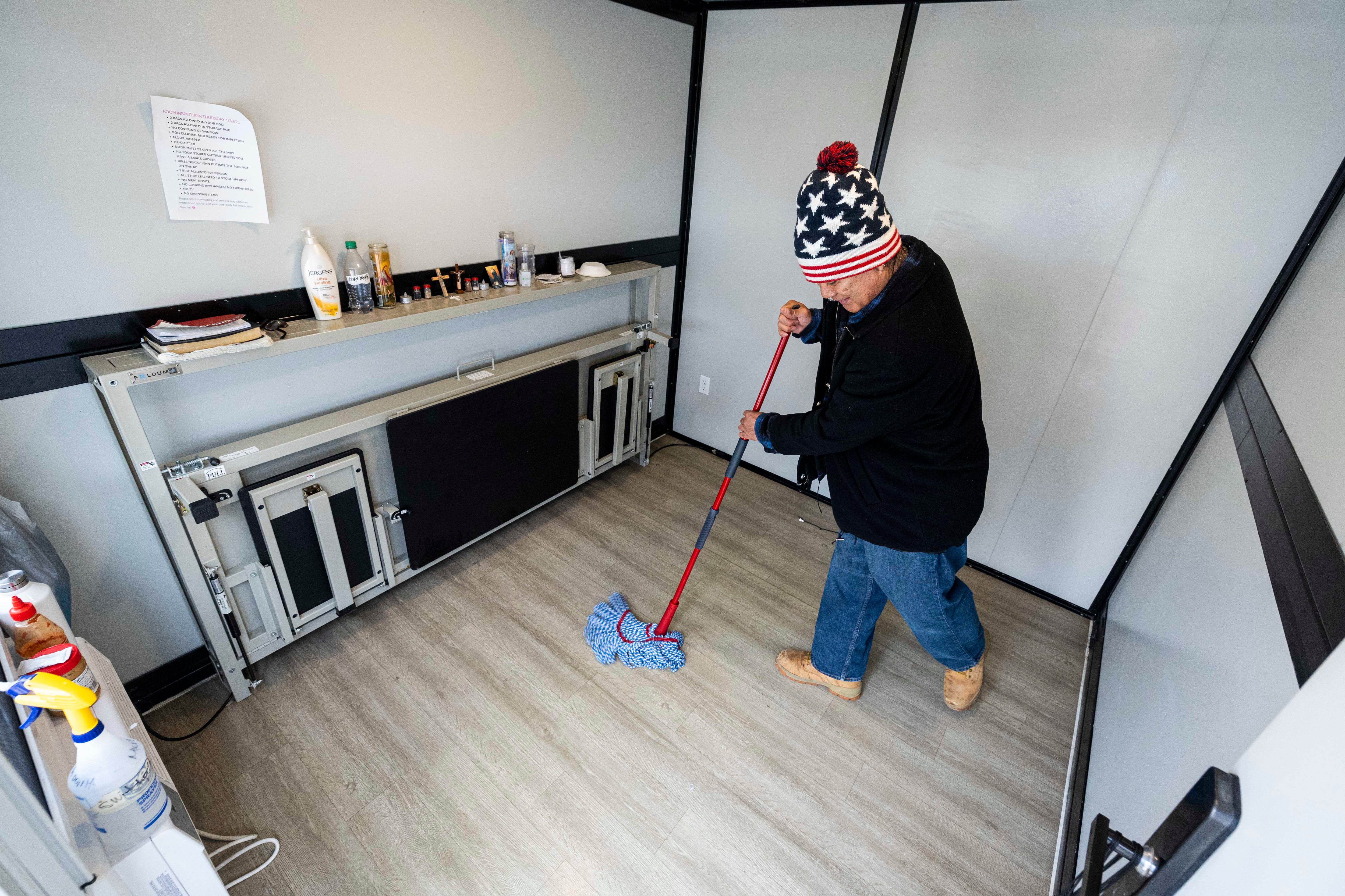 Dixie Nennis mops the floor of his microshelter unit at a microshelter community operated by Switchpoint in Salt Lake City on Thursday.