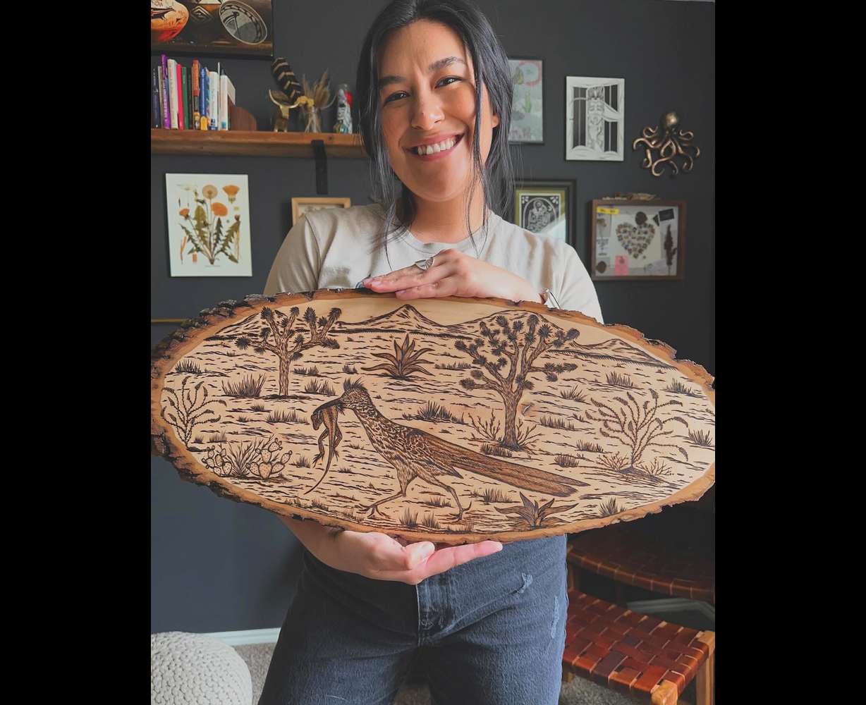 Miriam Gutierrez holds up an original artwork she made with a wood-burning technique.