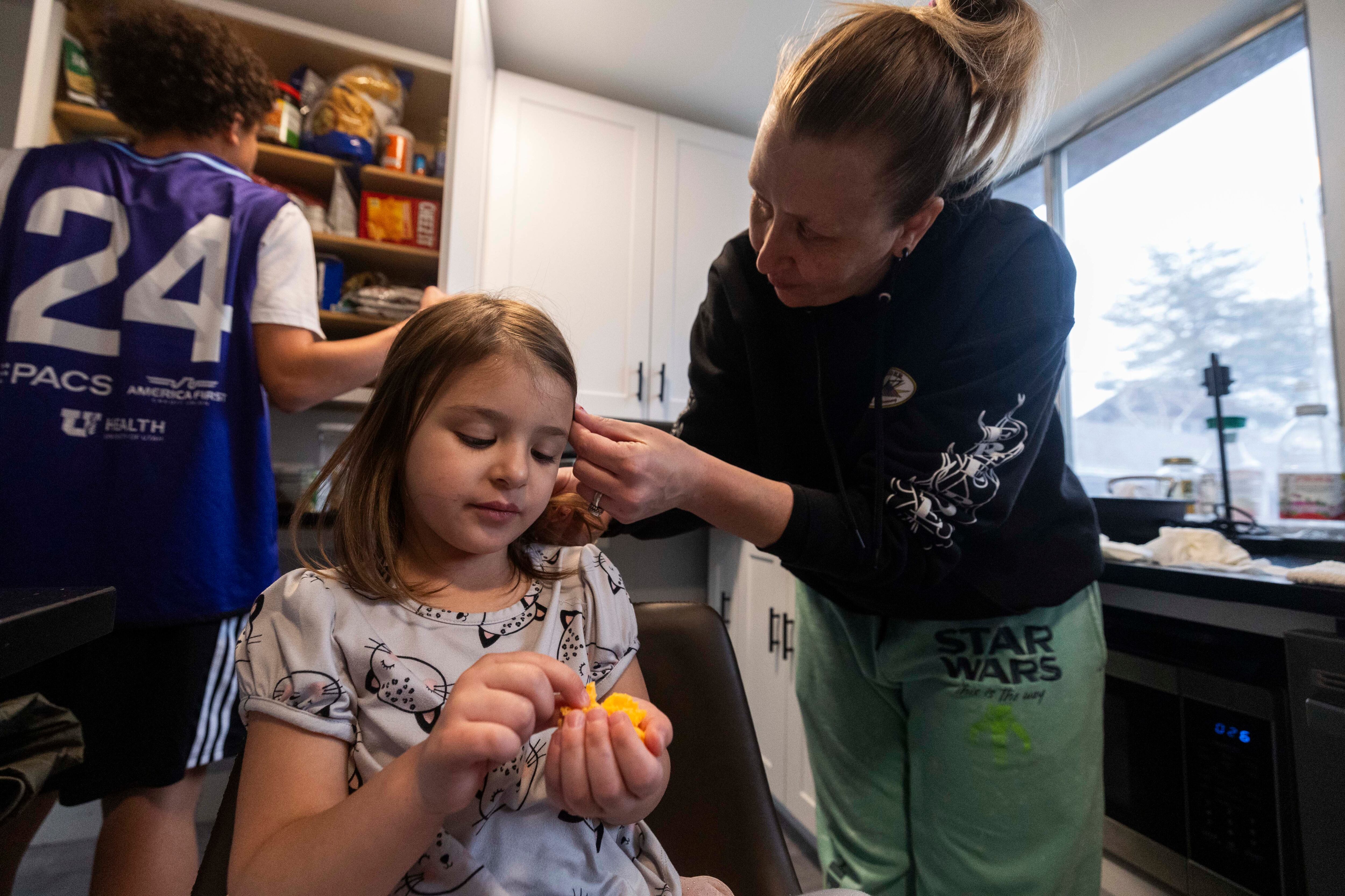 Amelia Diaz, 4, left, eats shredded cheese while her mother, Emily Diaz, right, fixes her hair, at their home in Midvale on Tuesday. Over the last few years, the Diaz family has experienced an increase in income which has highlighted the difficulties of transitioning away from welfare benefits without losing all of the benefits at once.