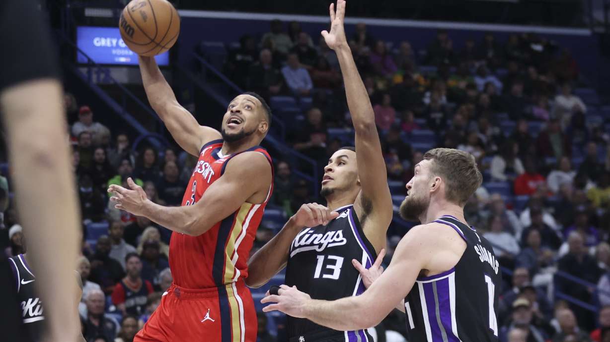 New Orleans Pelicans guard CJ McCollum, left, gets past Sacramento Kings forwards Keegan Murray (13) and Domantas Sabonis (11) for a layup during the first half of an NBA basketball game in New Orleans, Thursday, Feb. 13, 2025.