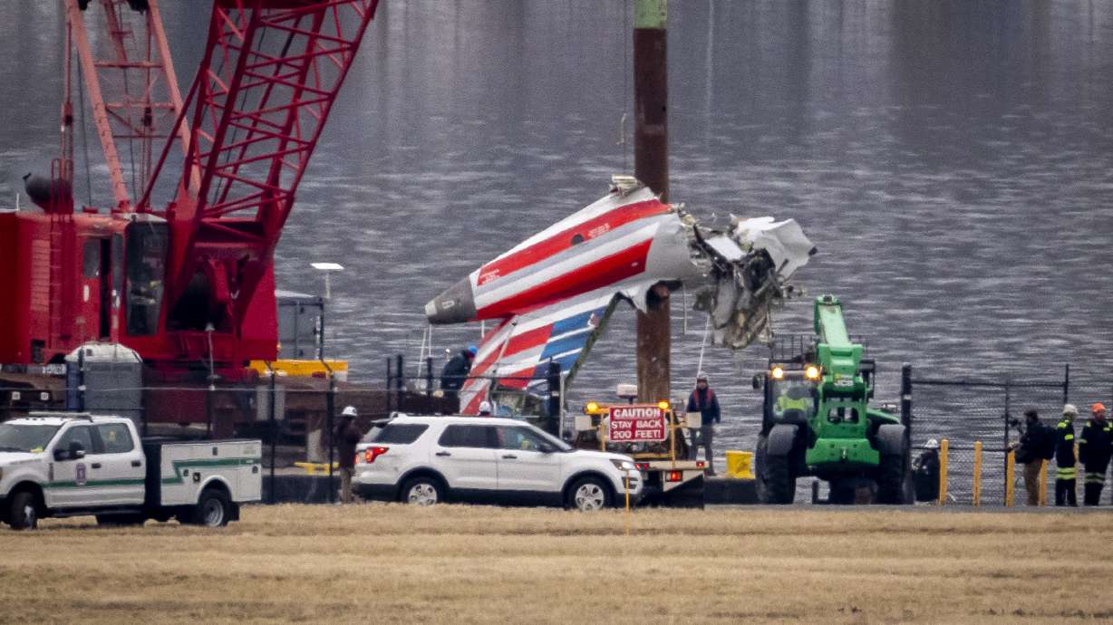 A crane offloads a piece of wreckage from a salvage vessel onto a flatbed truck, near the wreckage site in the Potomac River of a mid-air collision between an American Airlines jet and a Black Hawk helicopter, at Ronald Reagan Washington National Airport, Wednesday, Feb. 5, 2025, in Arlington, Va.